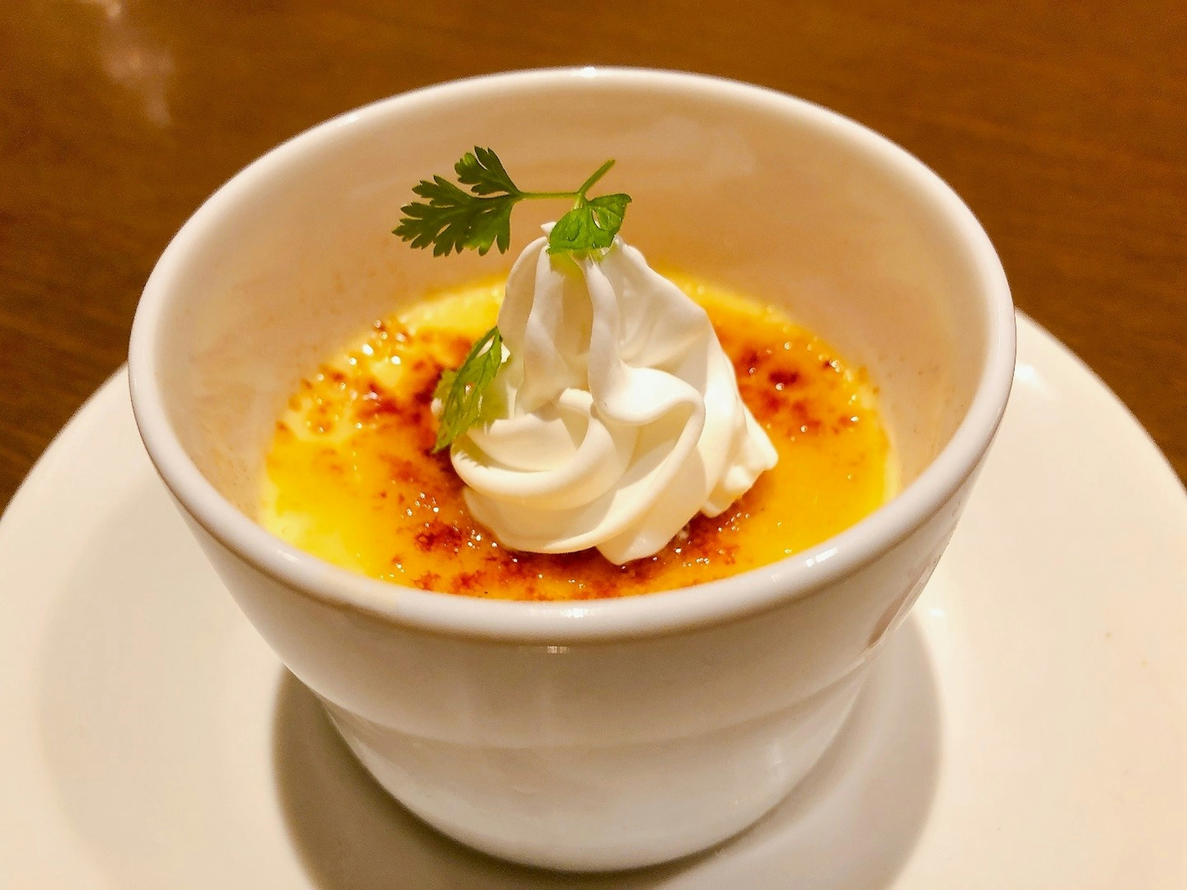 Postre crème brûlée en un tazón blanco cubierto con crema batida y una hoja de menta