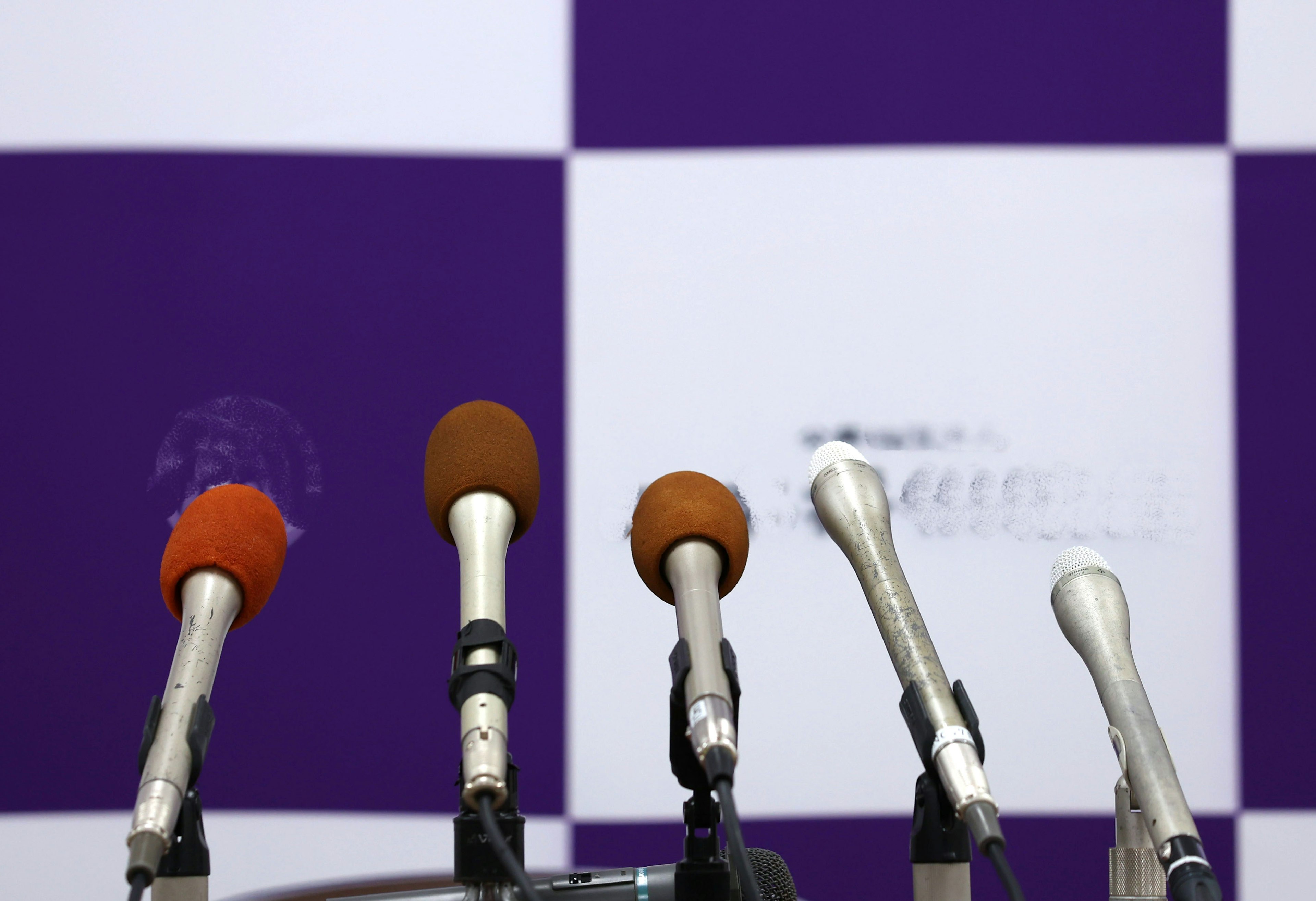 Microphones lined up in front of a purple and white background