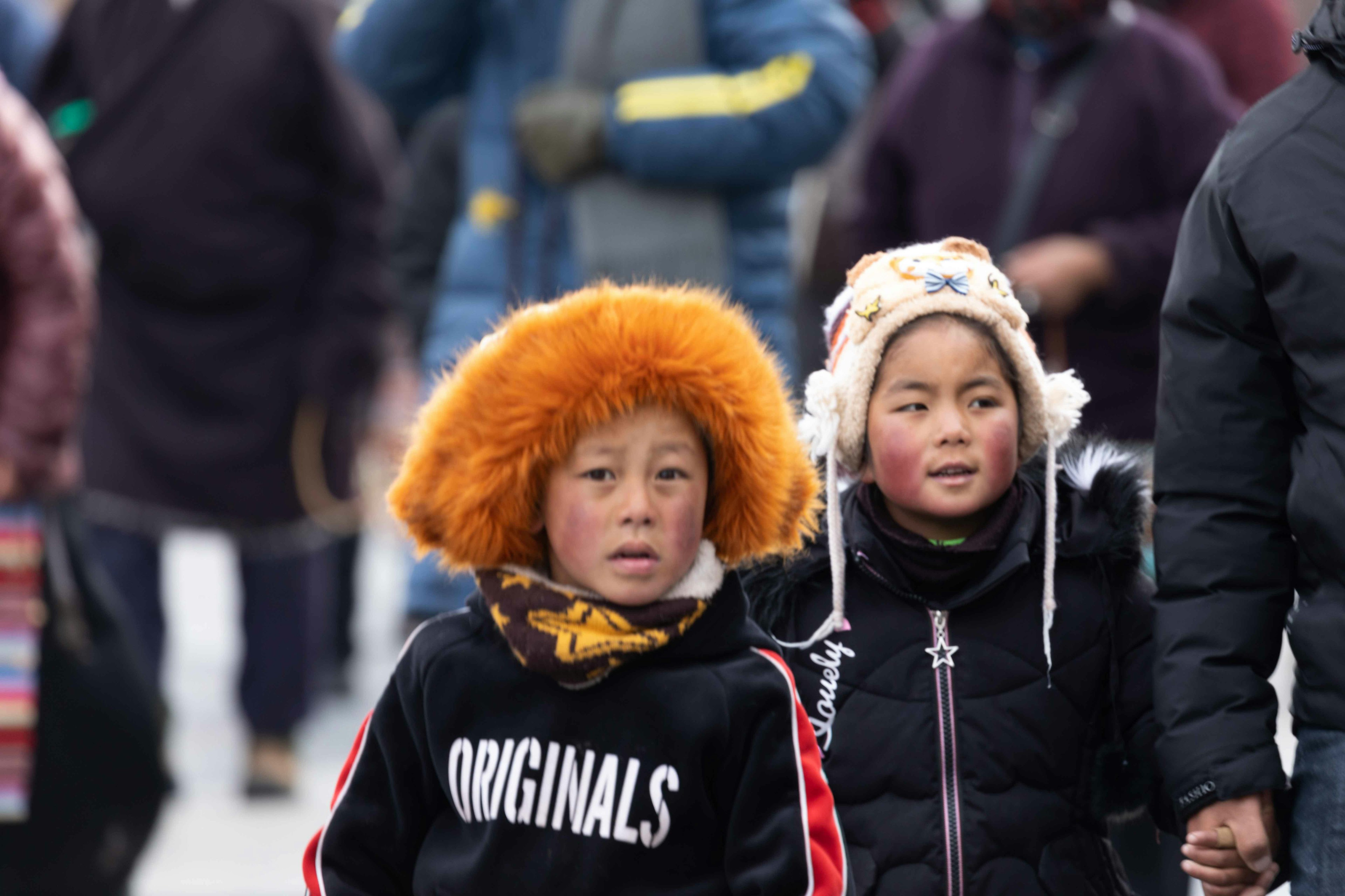 Un niño con un sombrero naranja y una niña con orejeras caminando de la mano