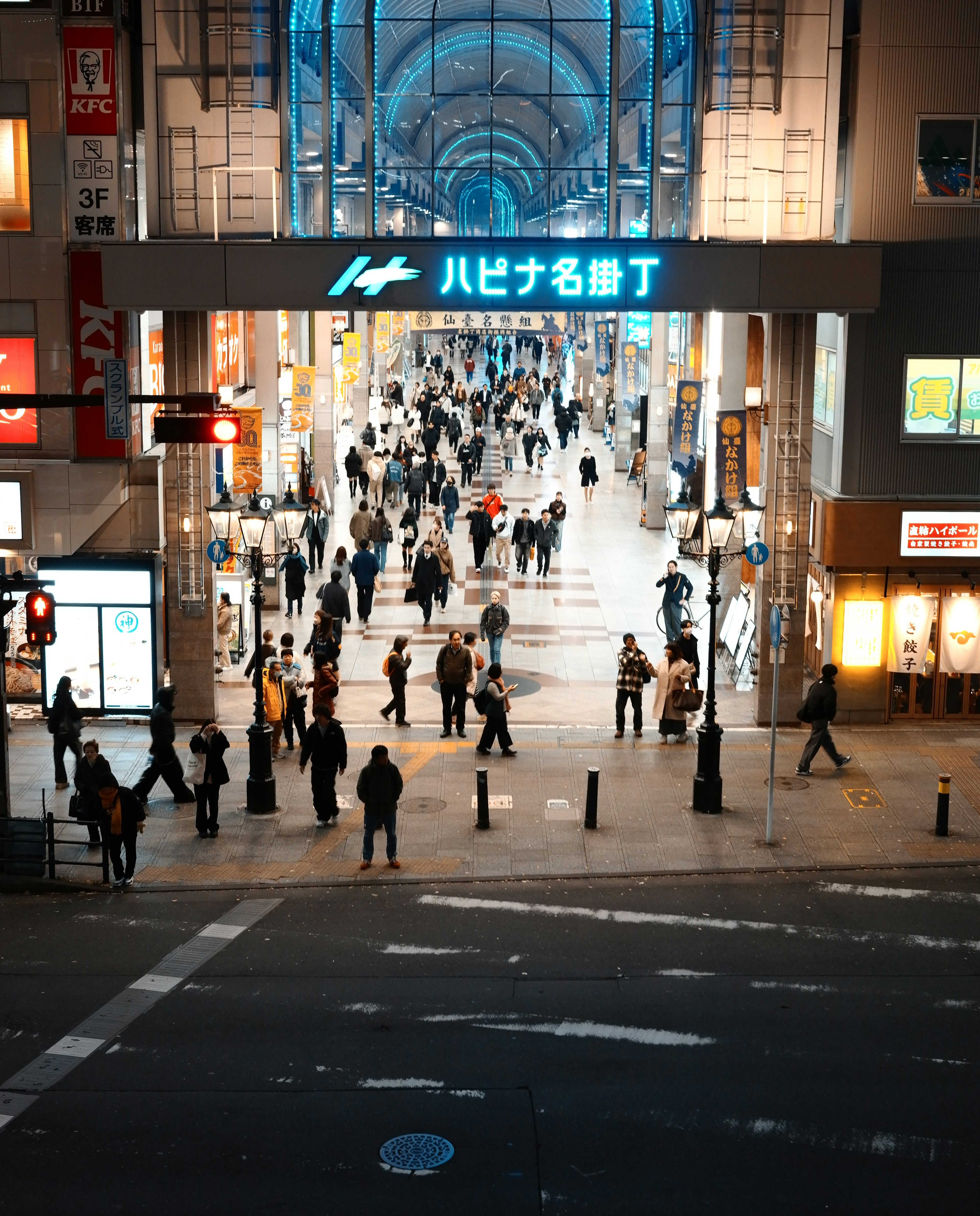 賑やかな通りに人々が行き交う様子 ハルヒナ名駅の入口が見える