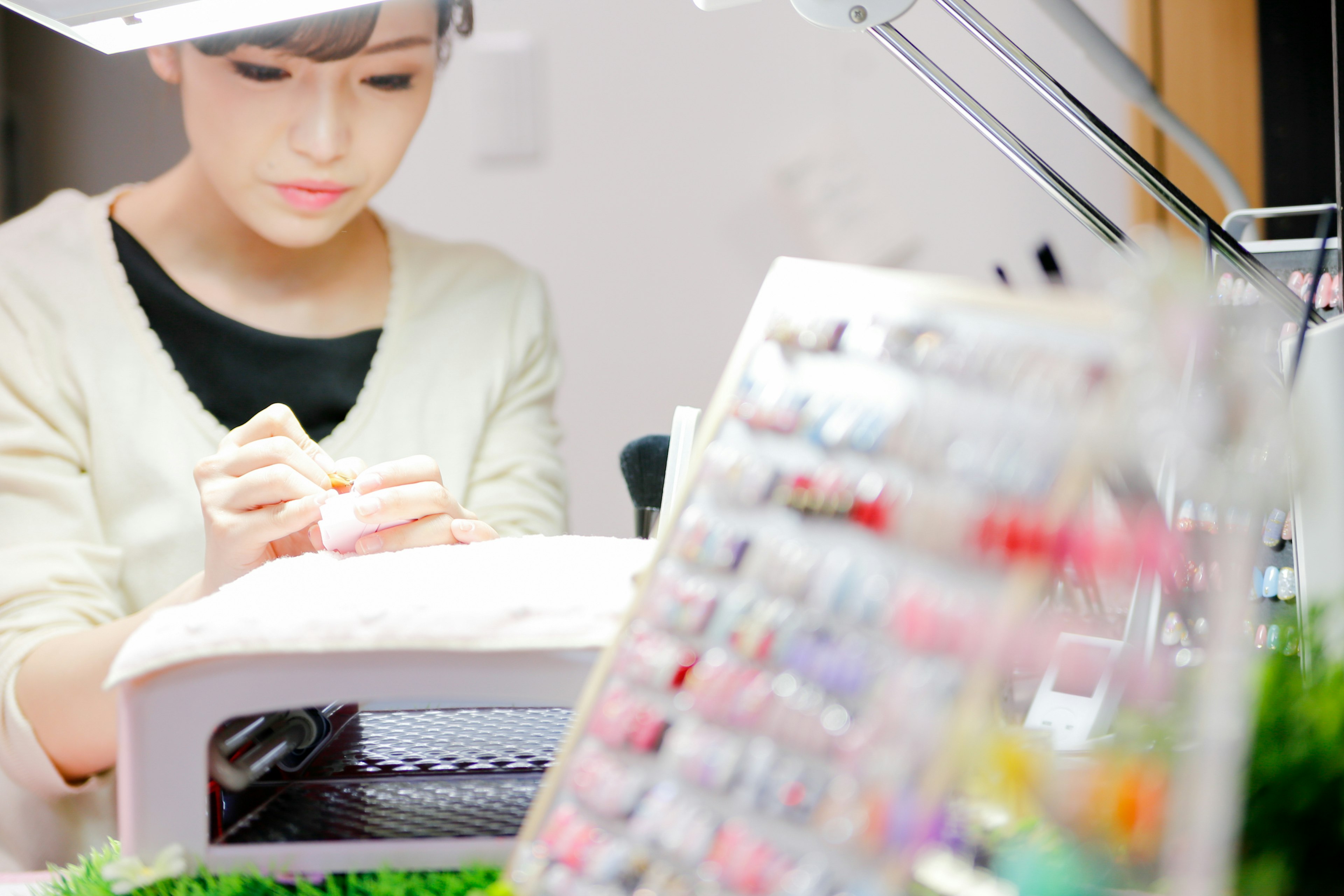 A woman applying nail art with a colorful nail polish display in the foreground