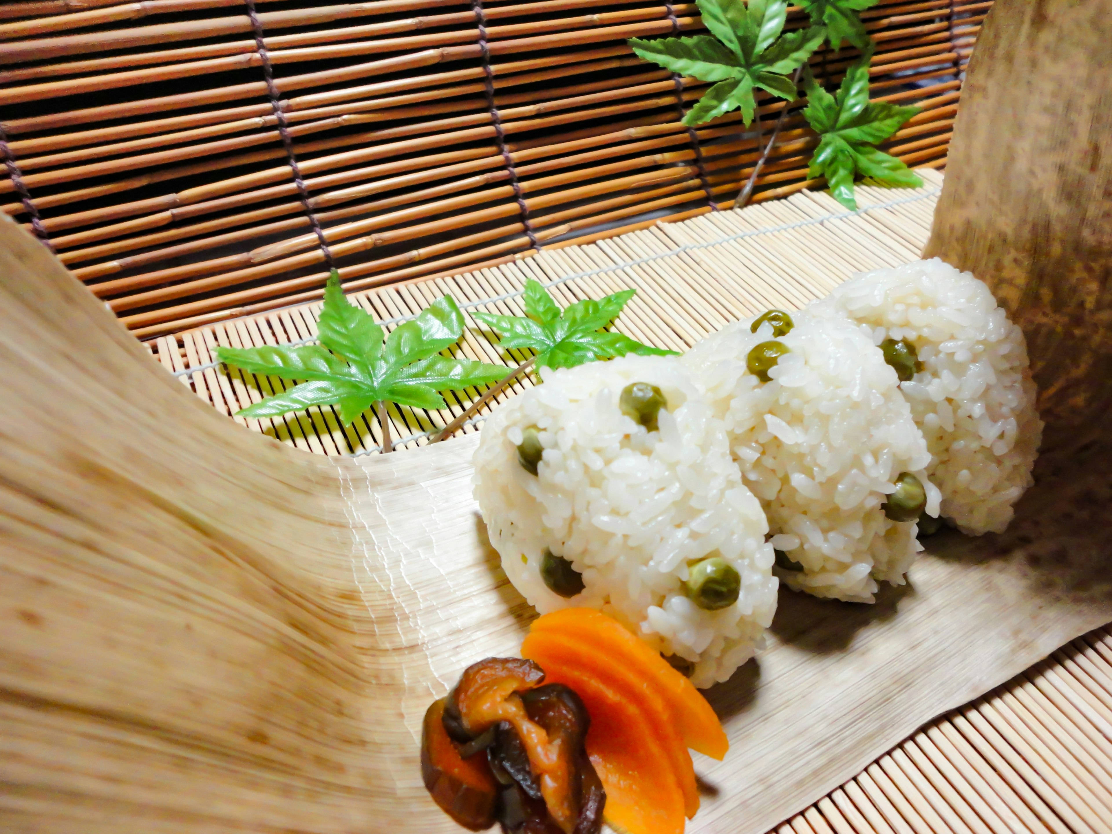 Tres bolas de arroz con guisantes verdes servidas sobre hojas de bambú con verduras