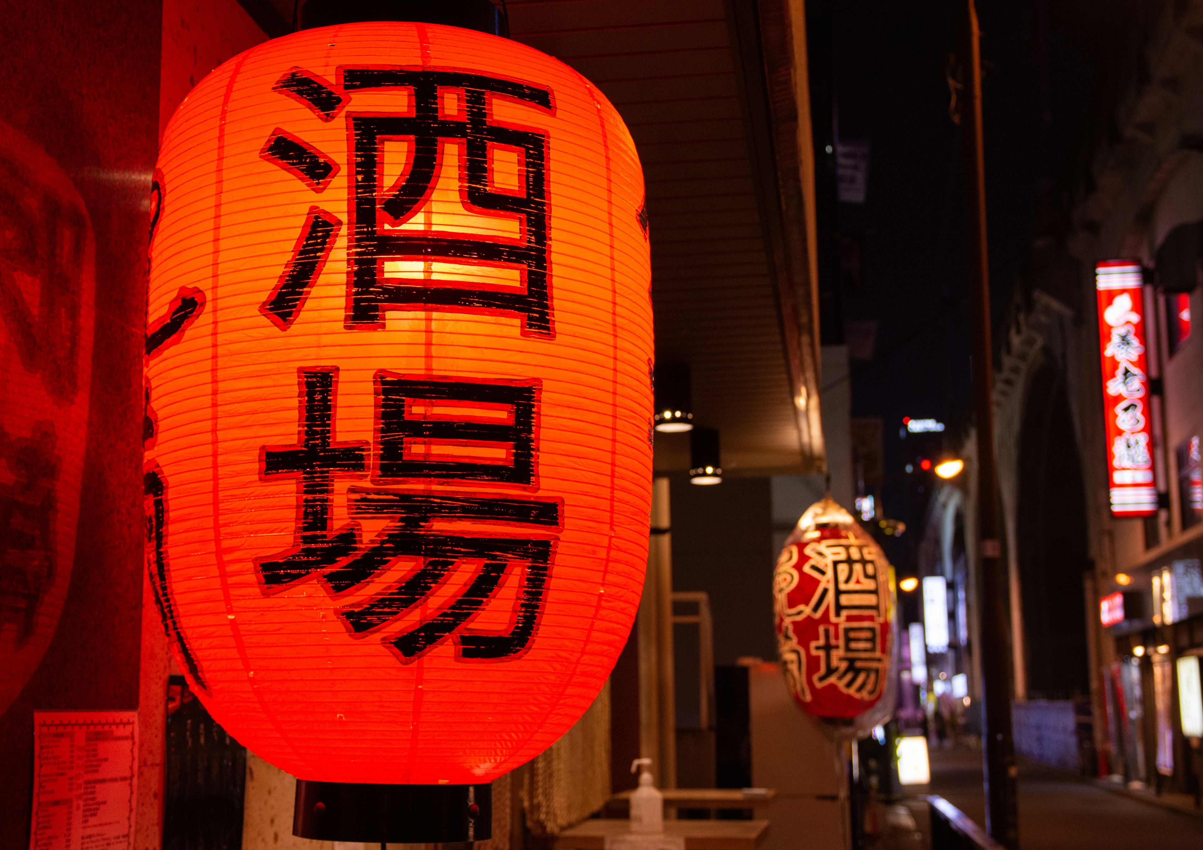 Faroles rojos iluminan una escena nocturna frente a un izakaya