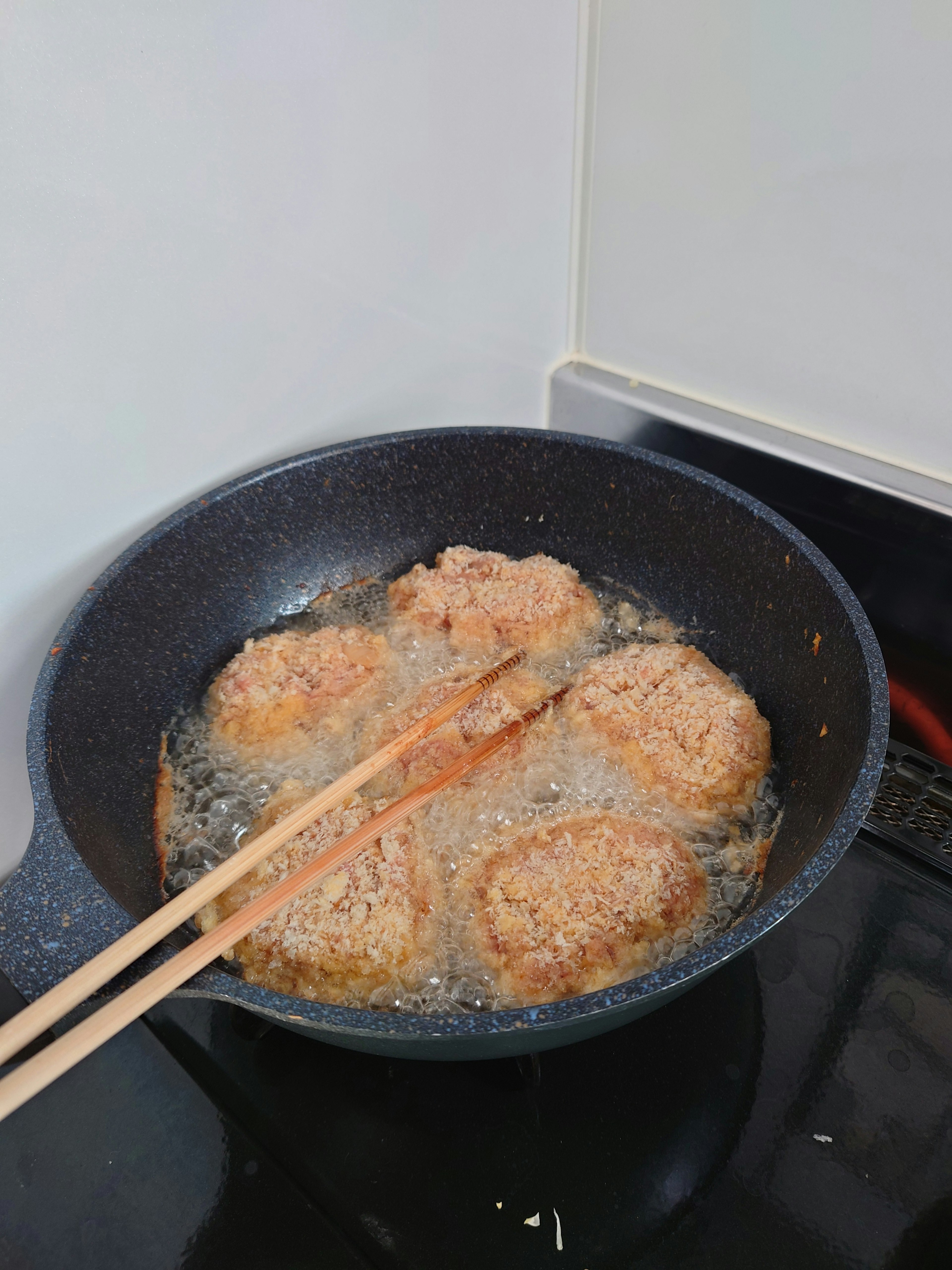 Croquettes frying in a pan with chopsticks