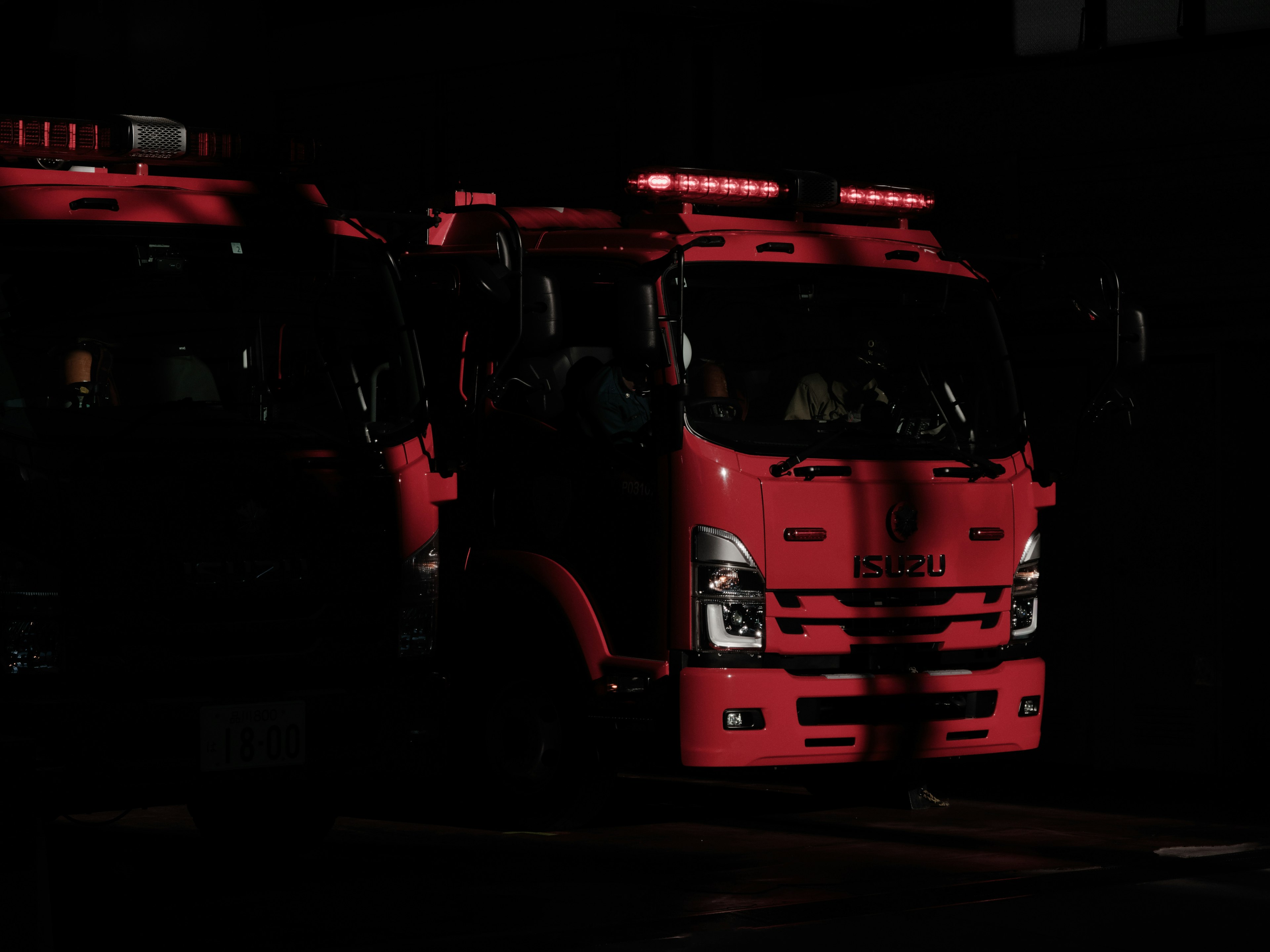 Camiones de bomberos rojos parcialmente iluminados contra un fondo oscuro