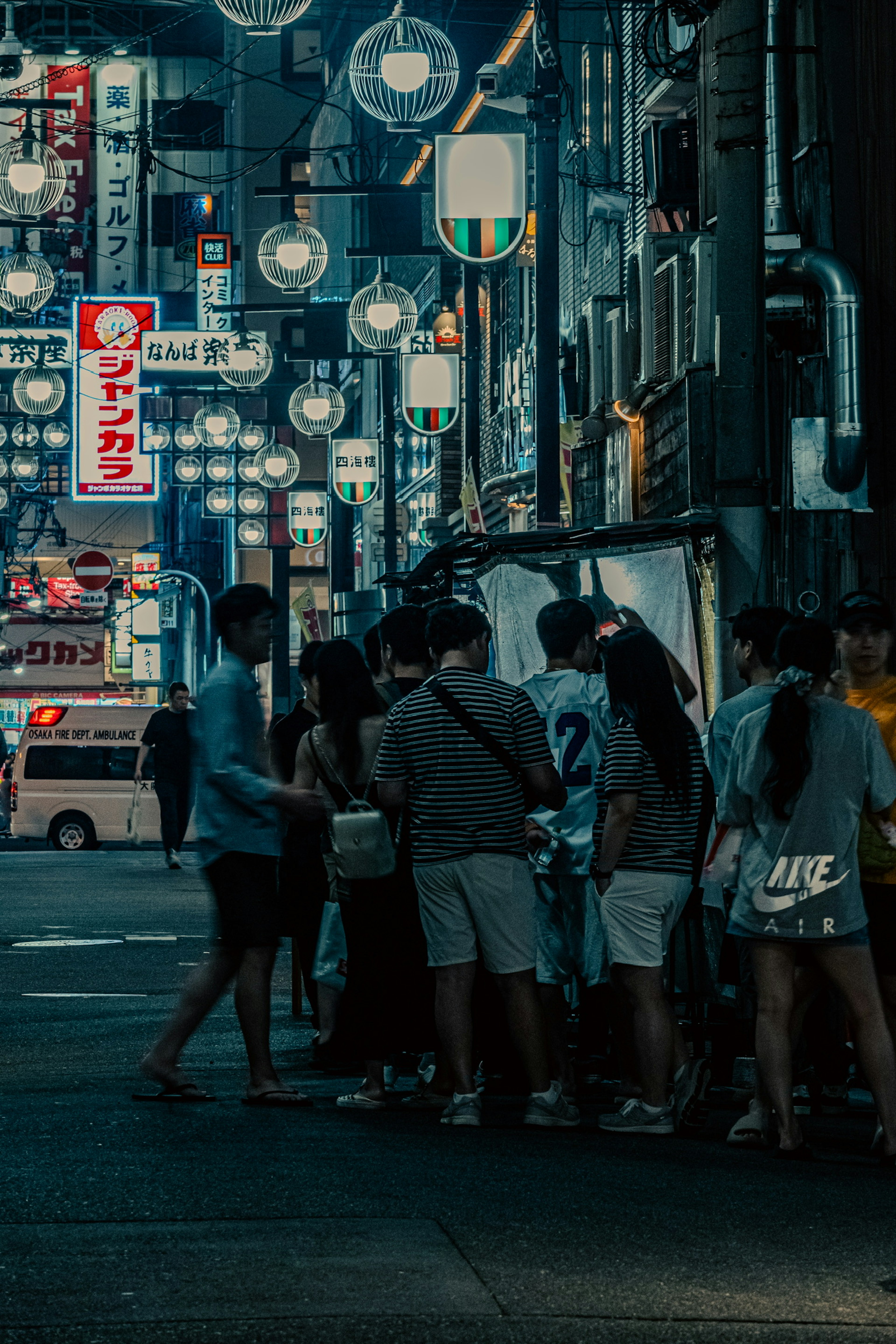 Group of people gathered around a food stall in a nighttime street scene