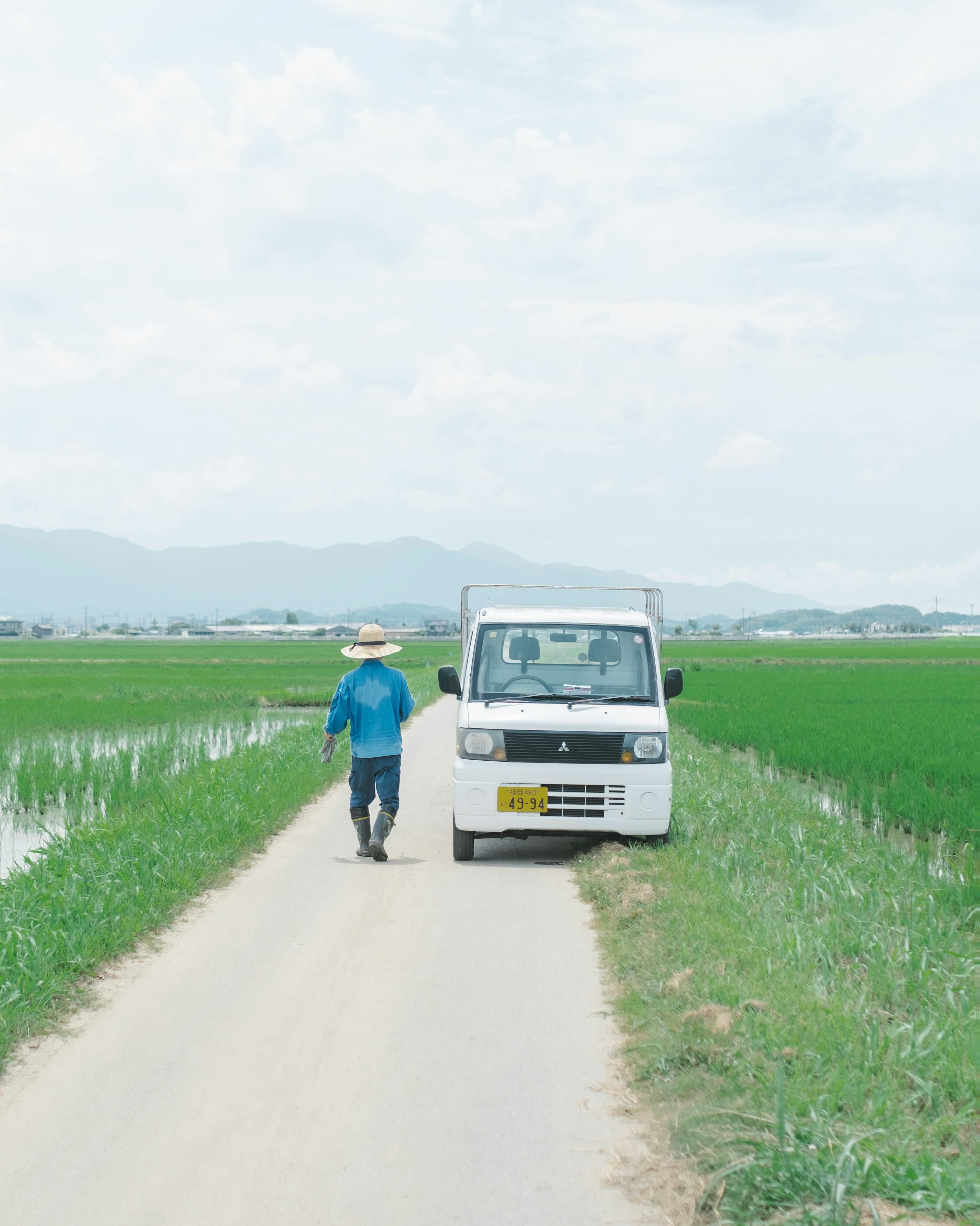 Un hombre caminando por un camino de tierra junto a campos de arroz con una camioneta blanca