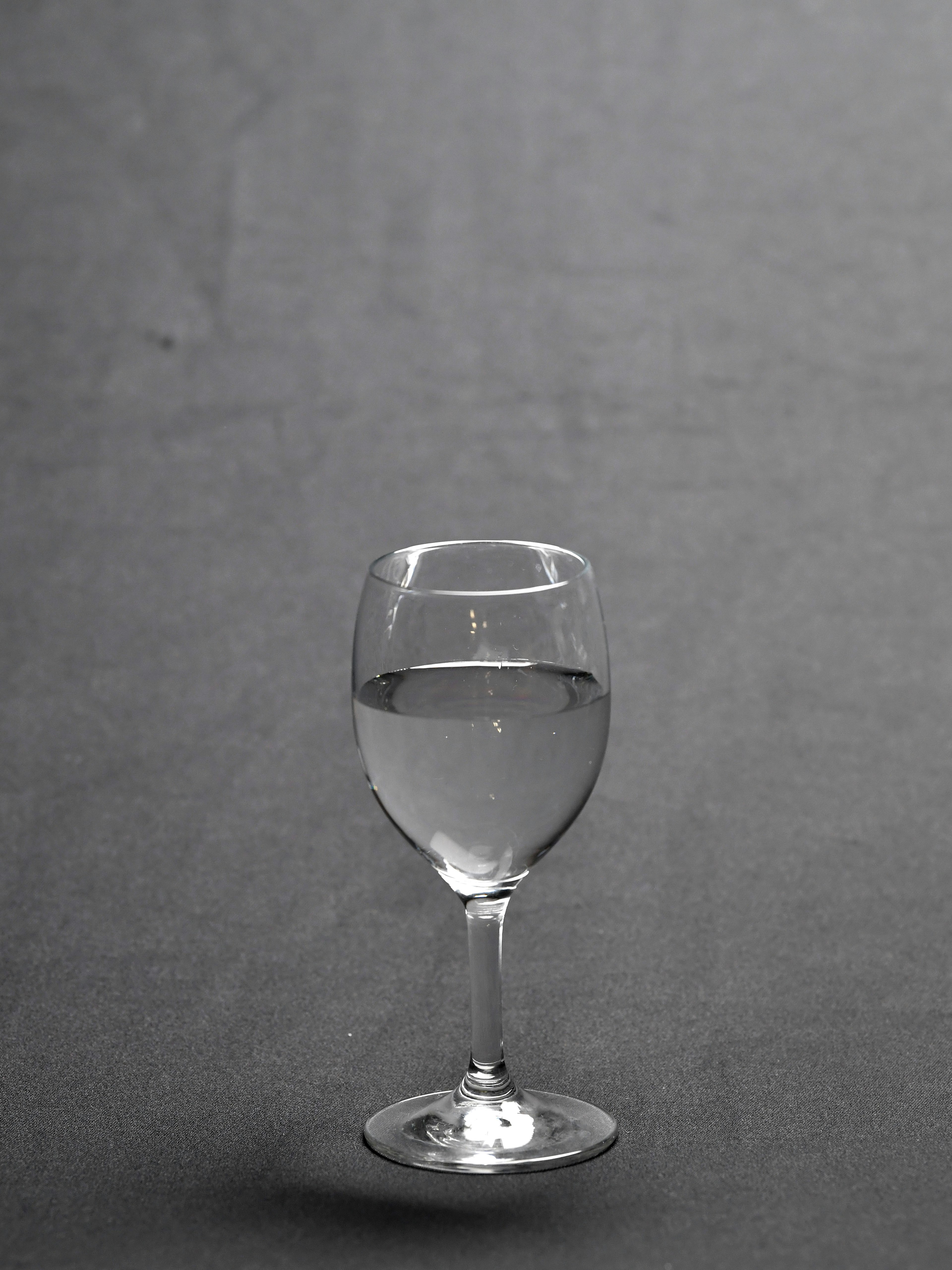 A wine glass filled with clear water set against a gray background