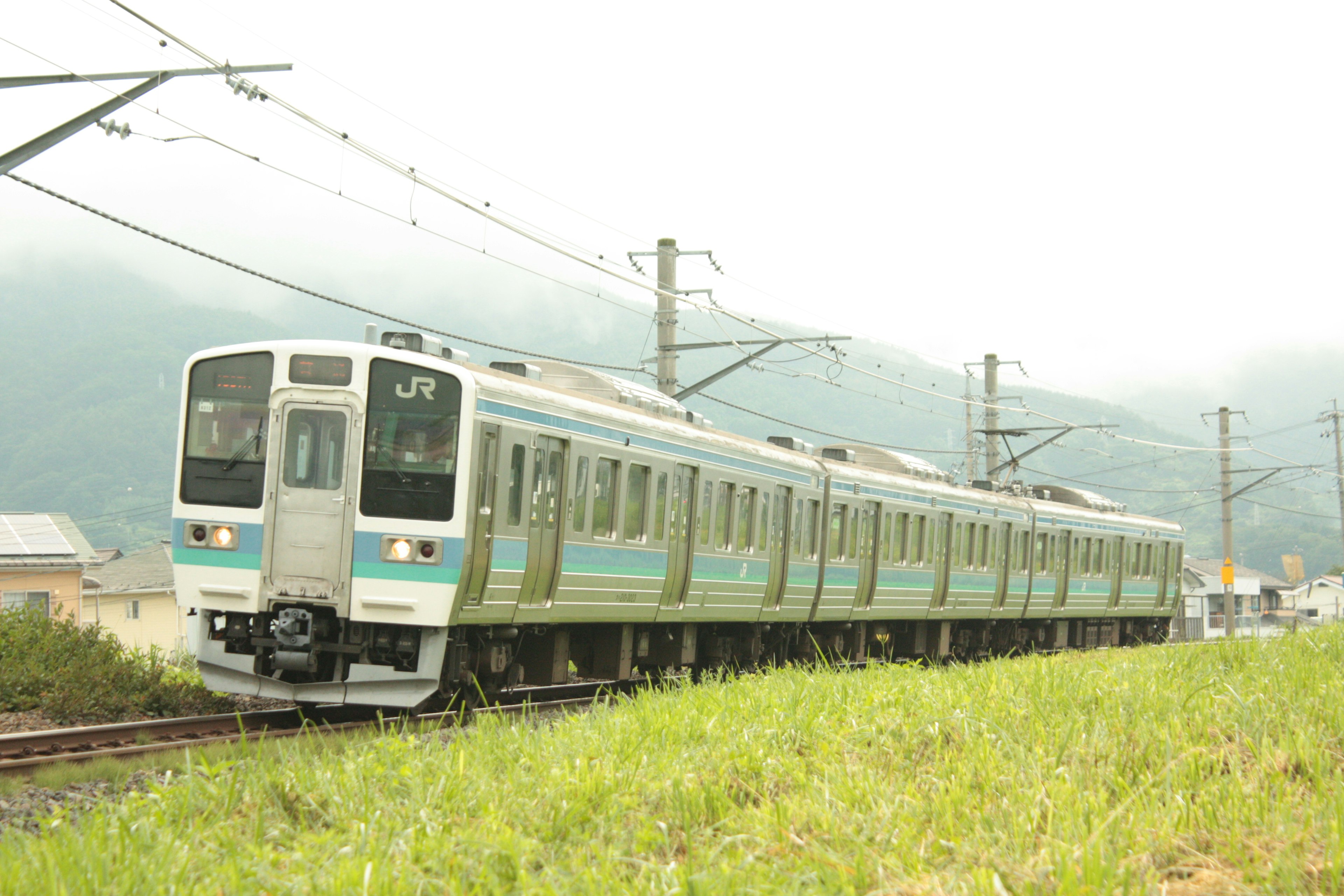 Tren japonés con rayas verdes que atraviesa un paisaje rural