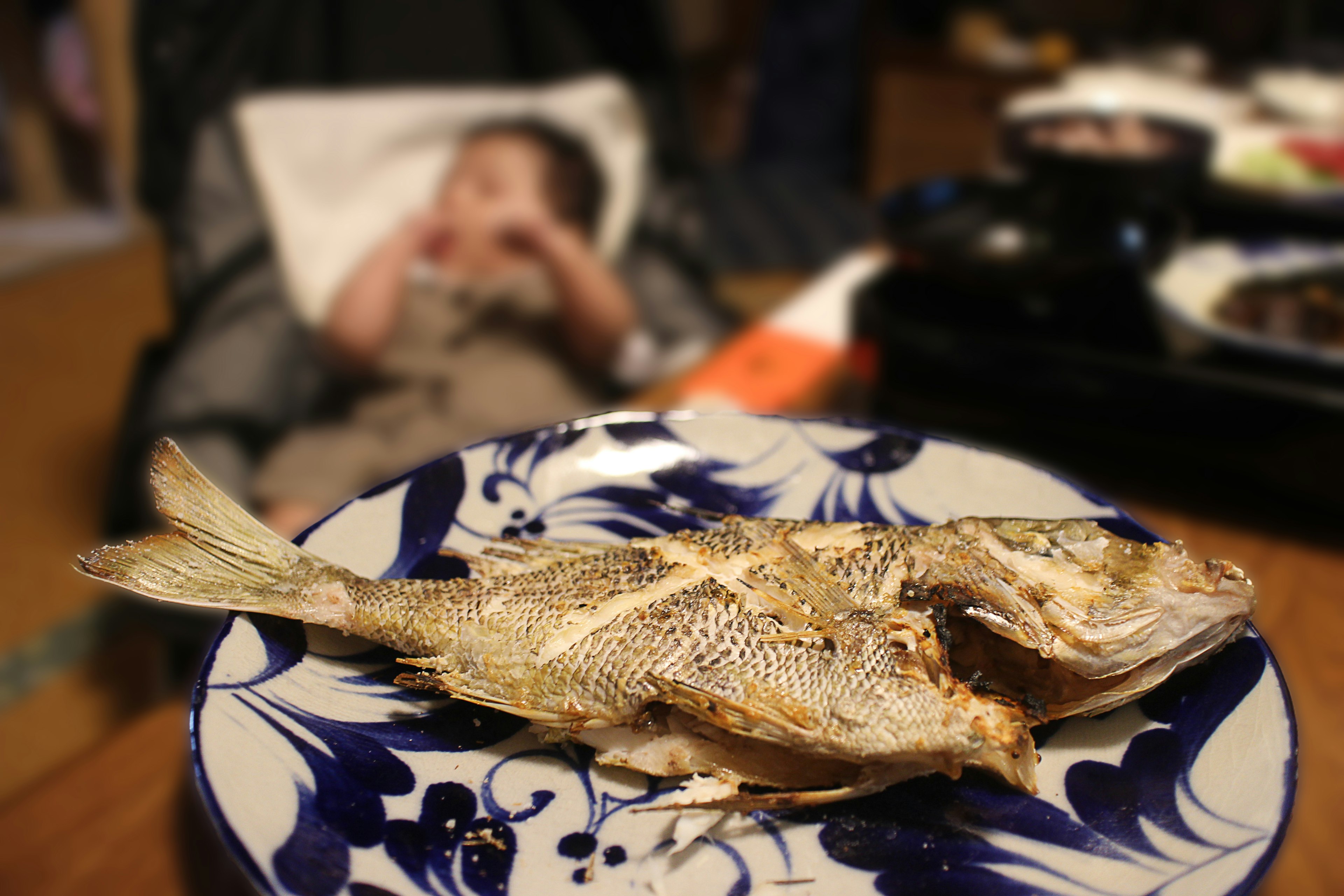 Pescado a la parrilla en un plato decorativo con un niño al fondo