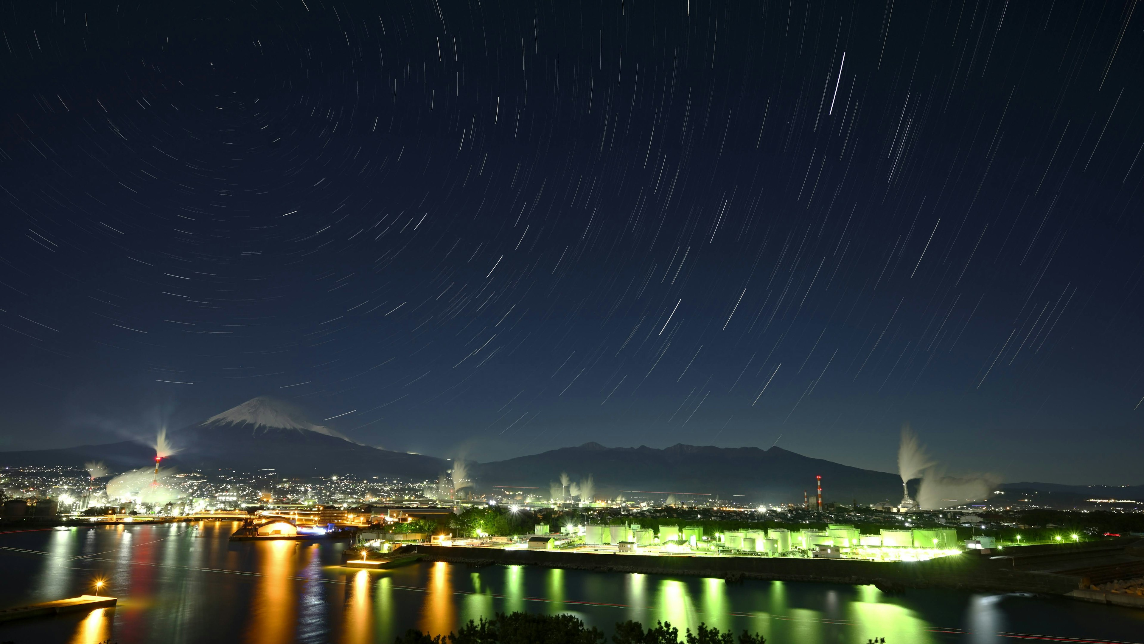 Schöne Landschaft mit fließenden Sternen über dem Fuji und Stadtlichtern bei Nacht