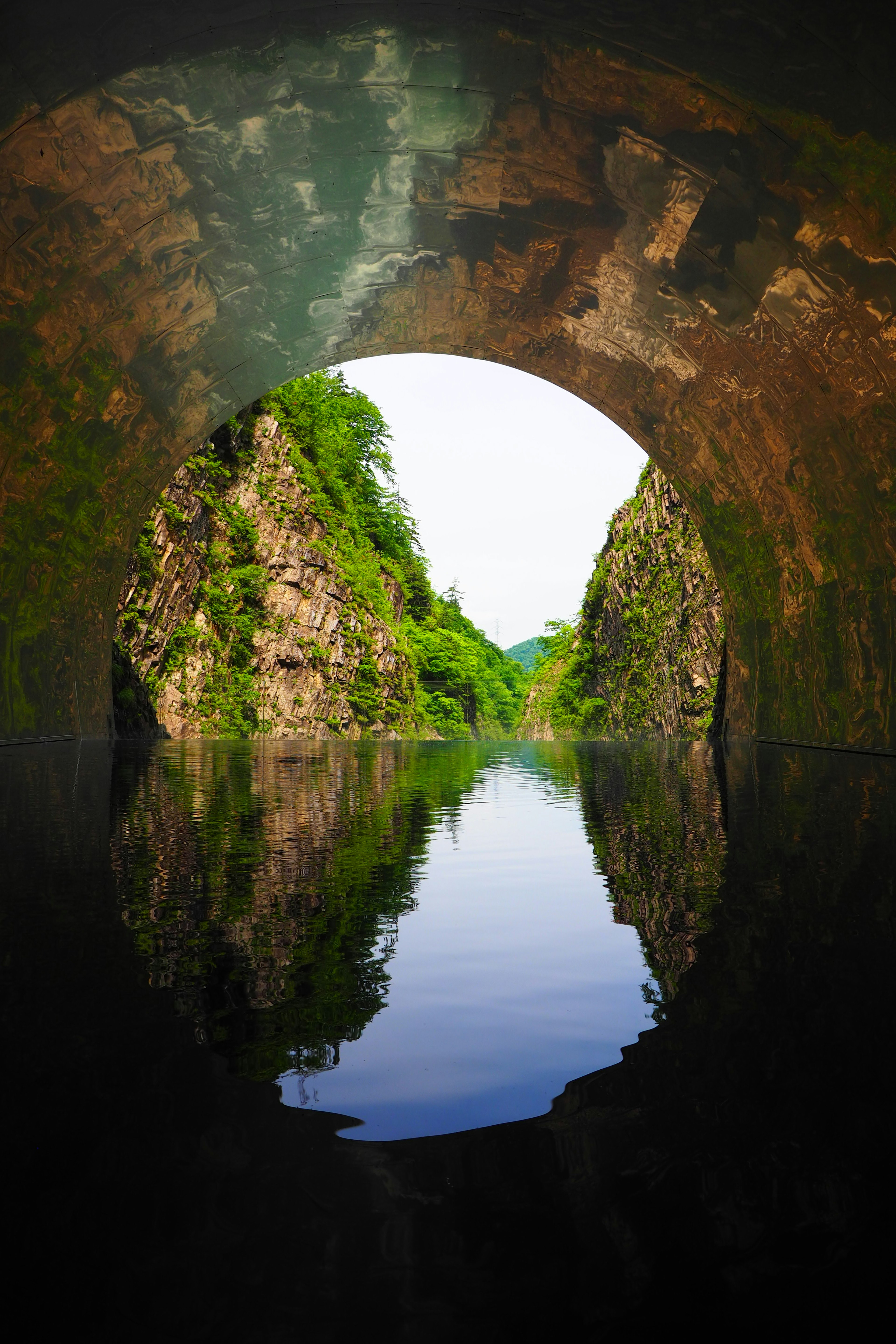 Vue d'une surface d'eau tranquille reflétant des parois rocheuses vertes depuis l'intérieur d'un tunnel