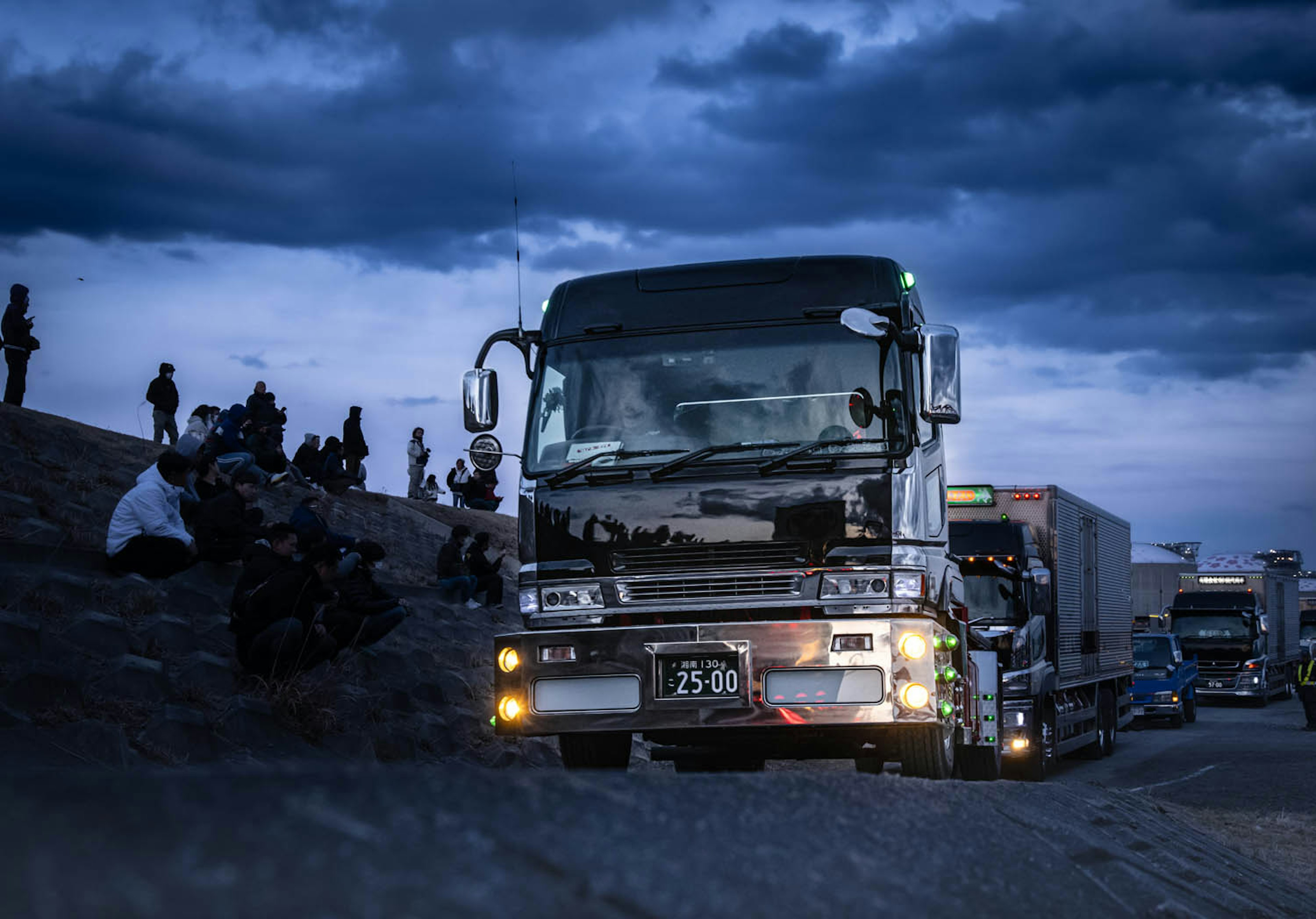 夜の高速道路でトラックが停車しているシーン 周囲には人々が座っている