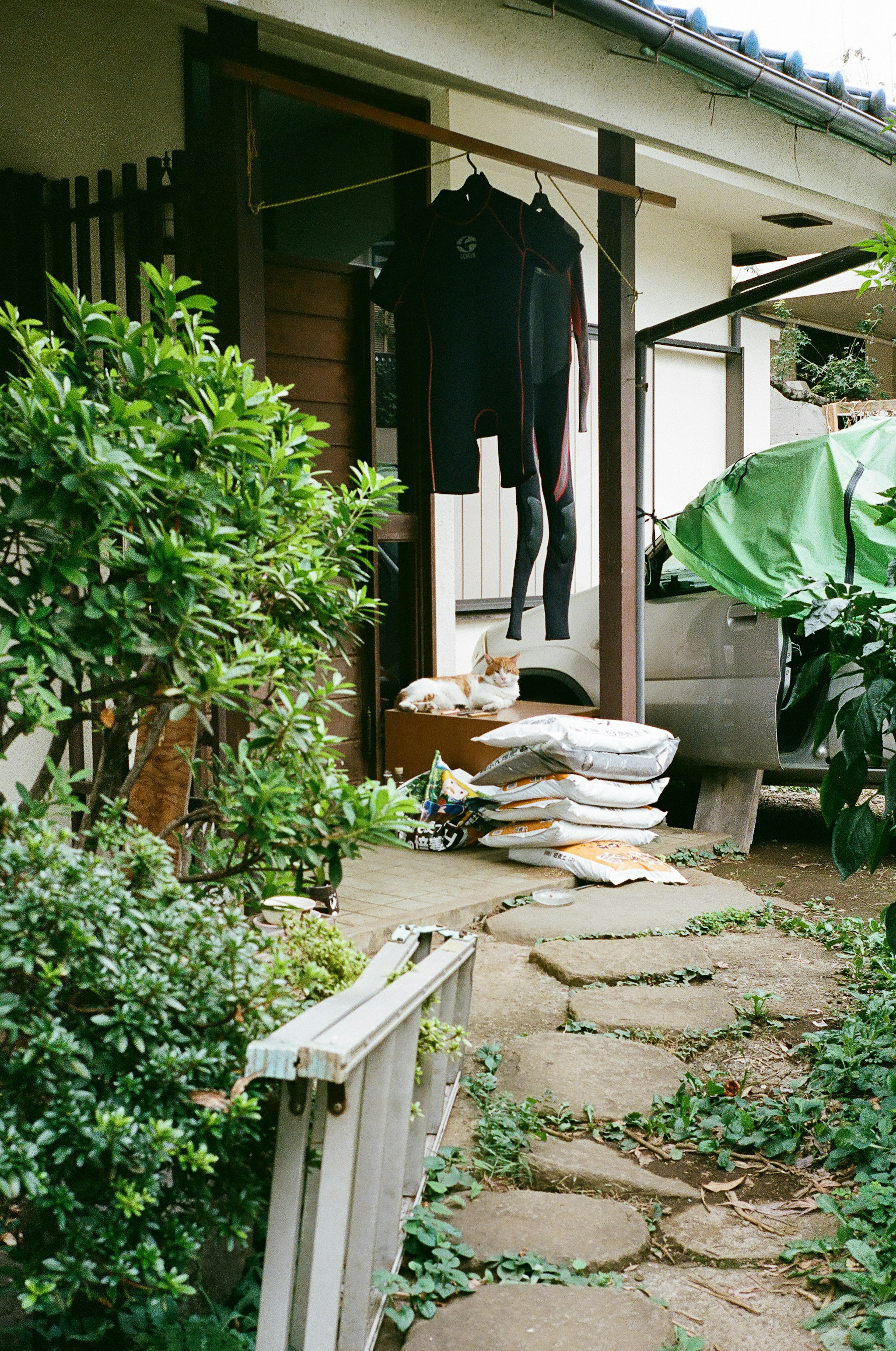 庭に干された黒い服と積まれた白いクッションがある家の入り口