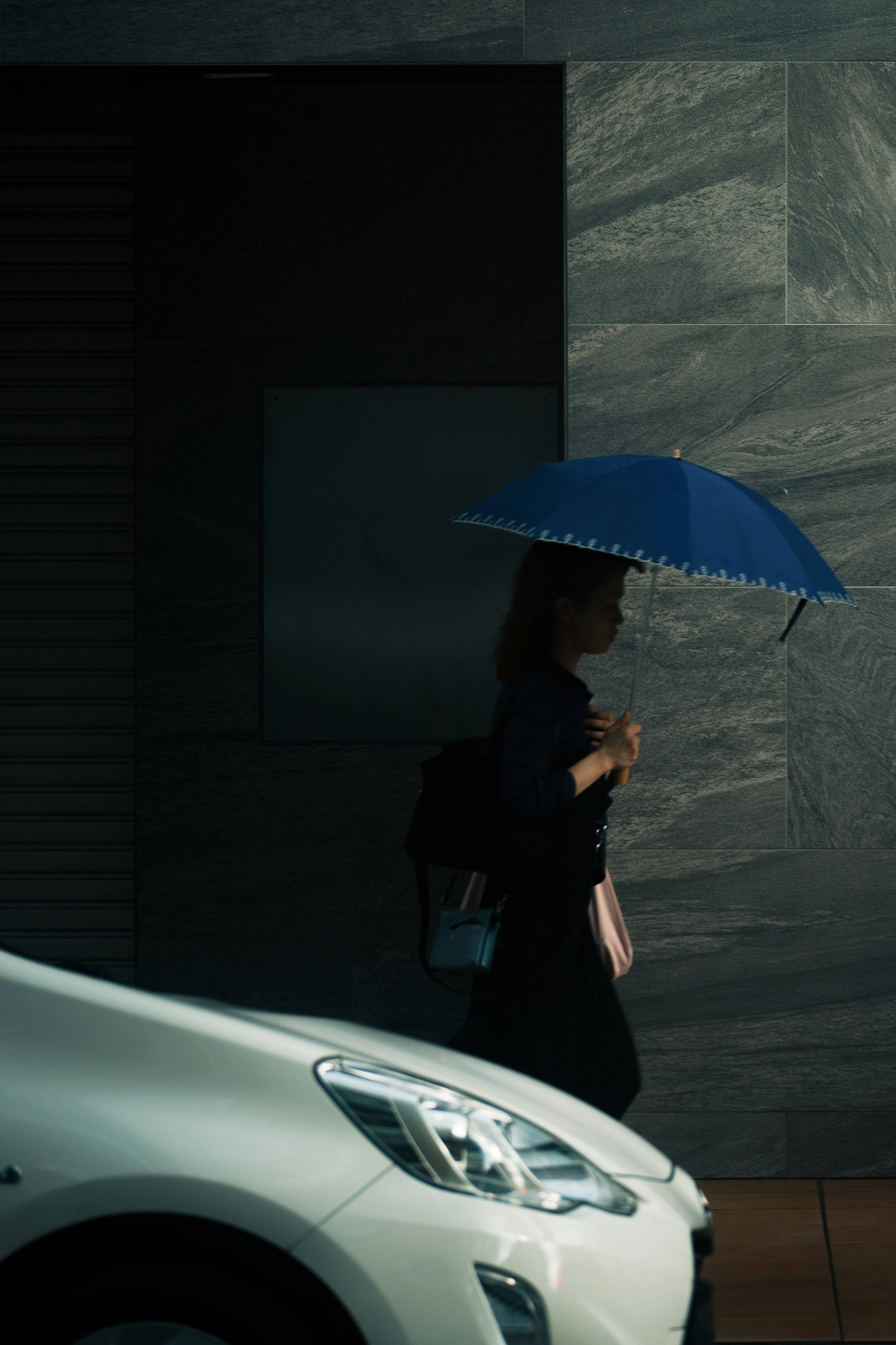 Une femme marchant avec un parapluie bleu à côté d'une voiture blanche