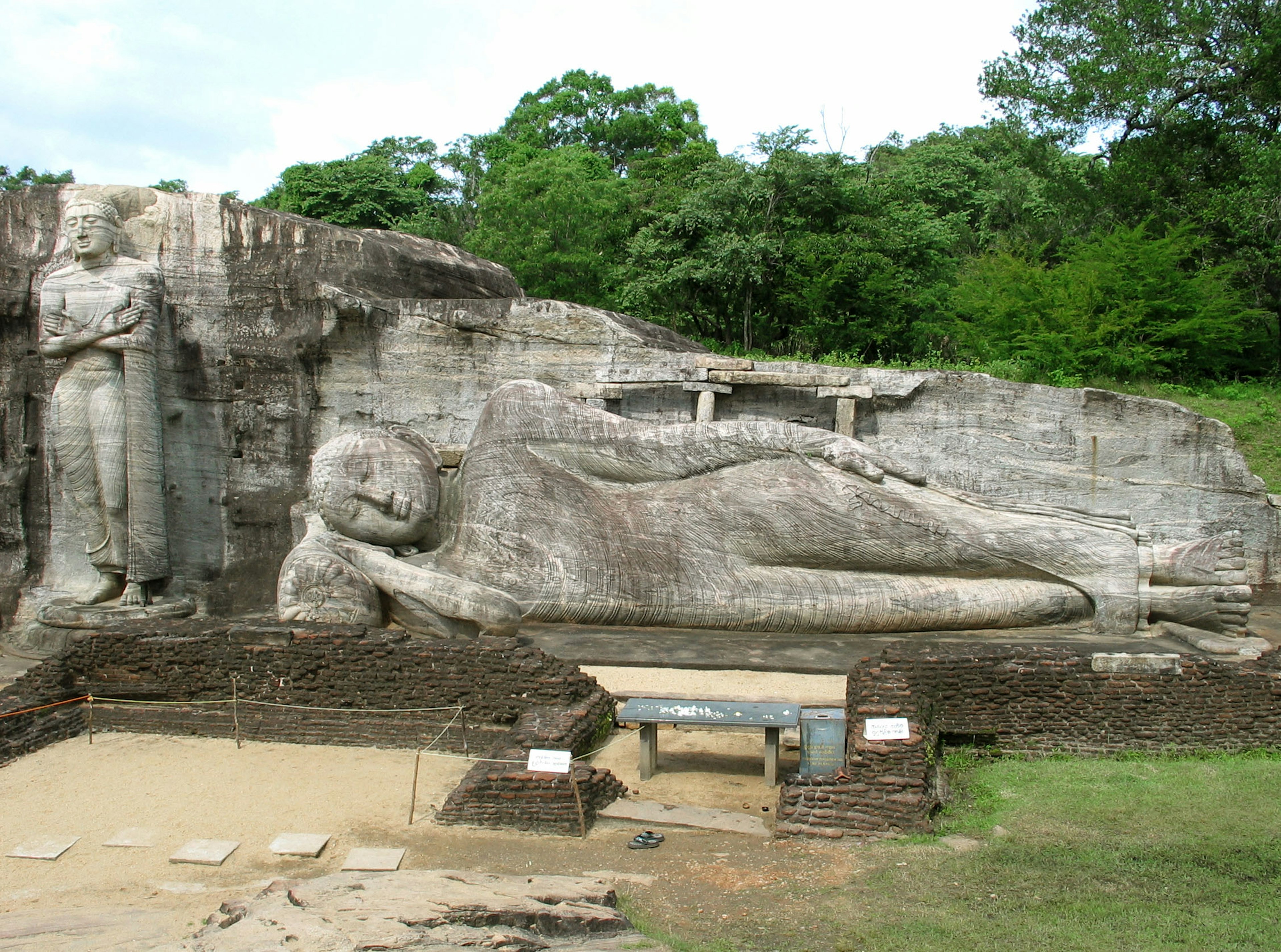 Gran estatua de Buda reclinado con una figura de Buda de pie adyacente tallada en un paisaje rocoso