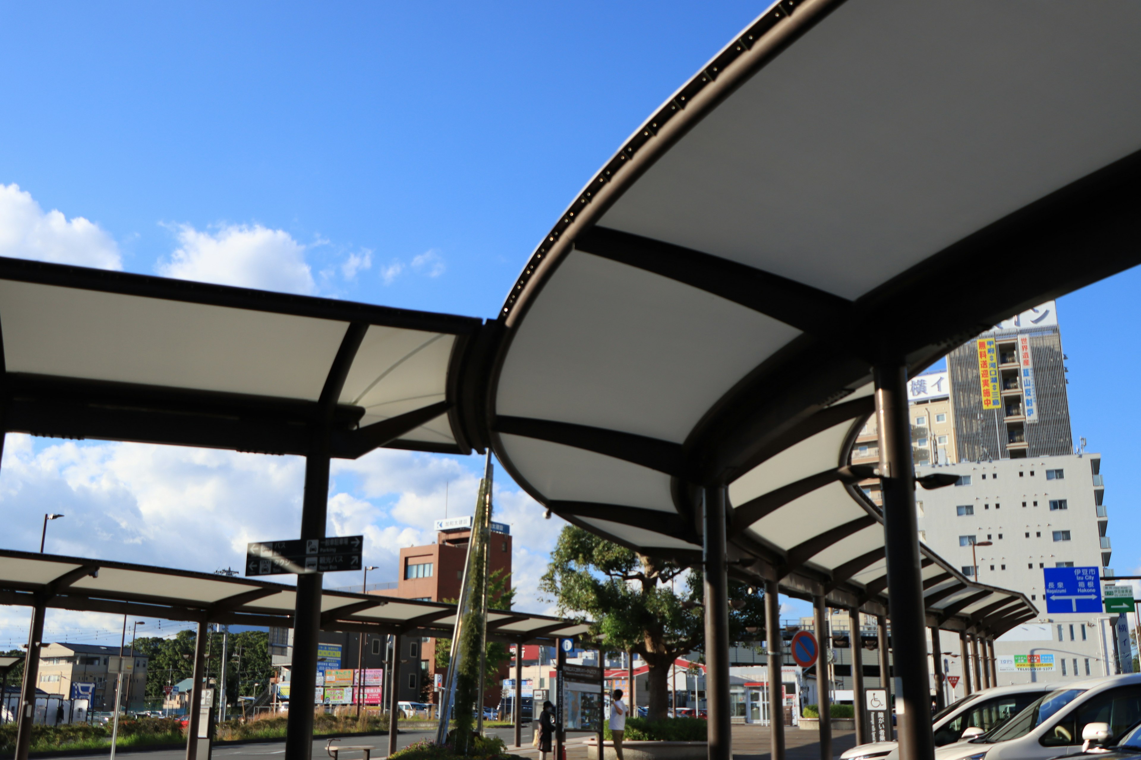 Abris de bus modernes avec toits incurvés sous un ciel bleu et bâtiments environnants