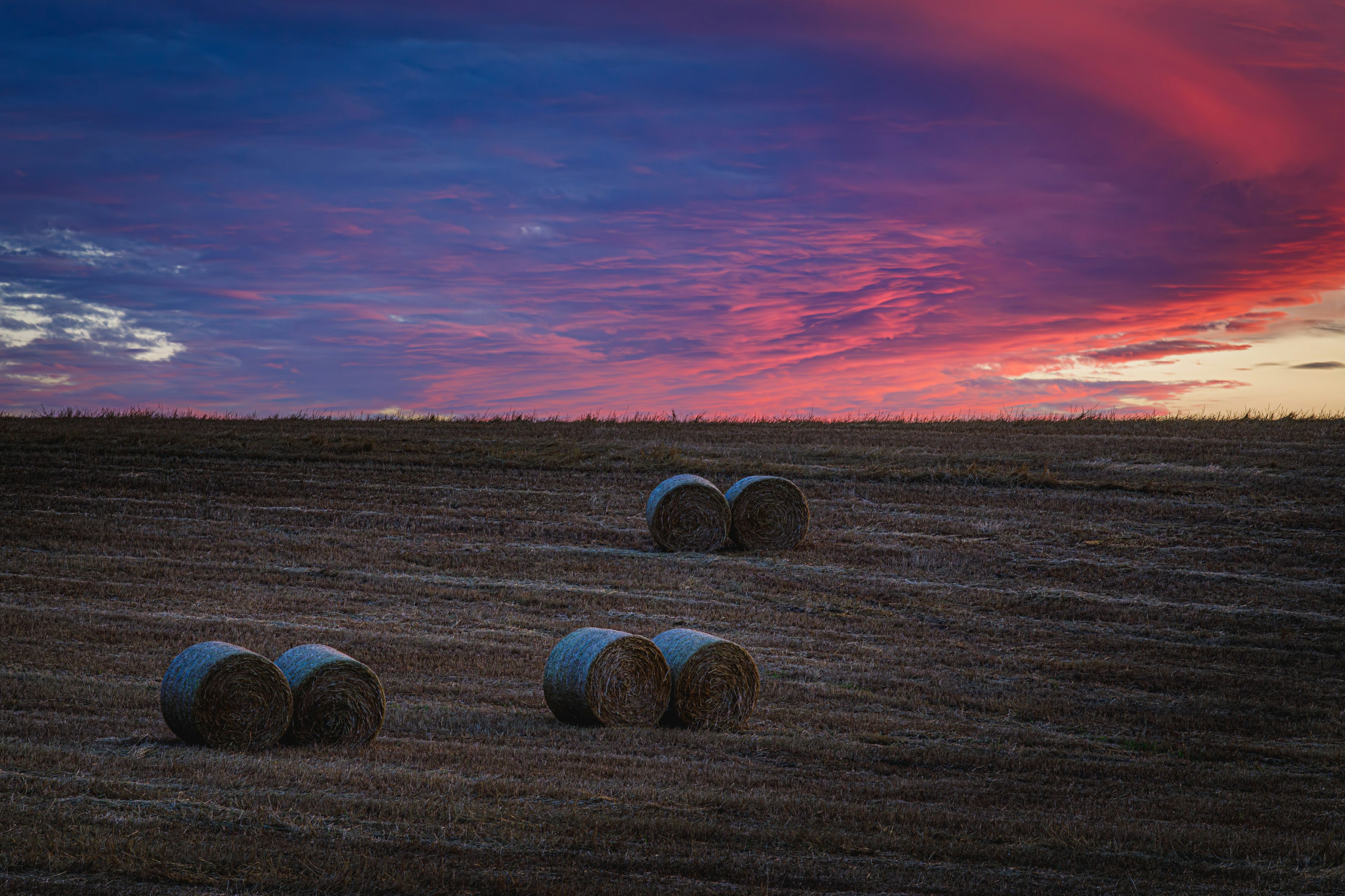 Bales of hay on a field under a colorful sunset sky