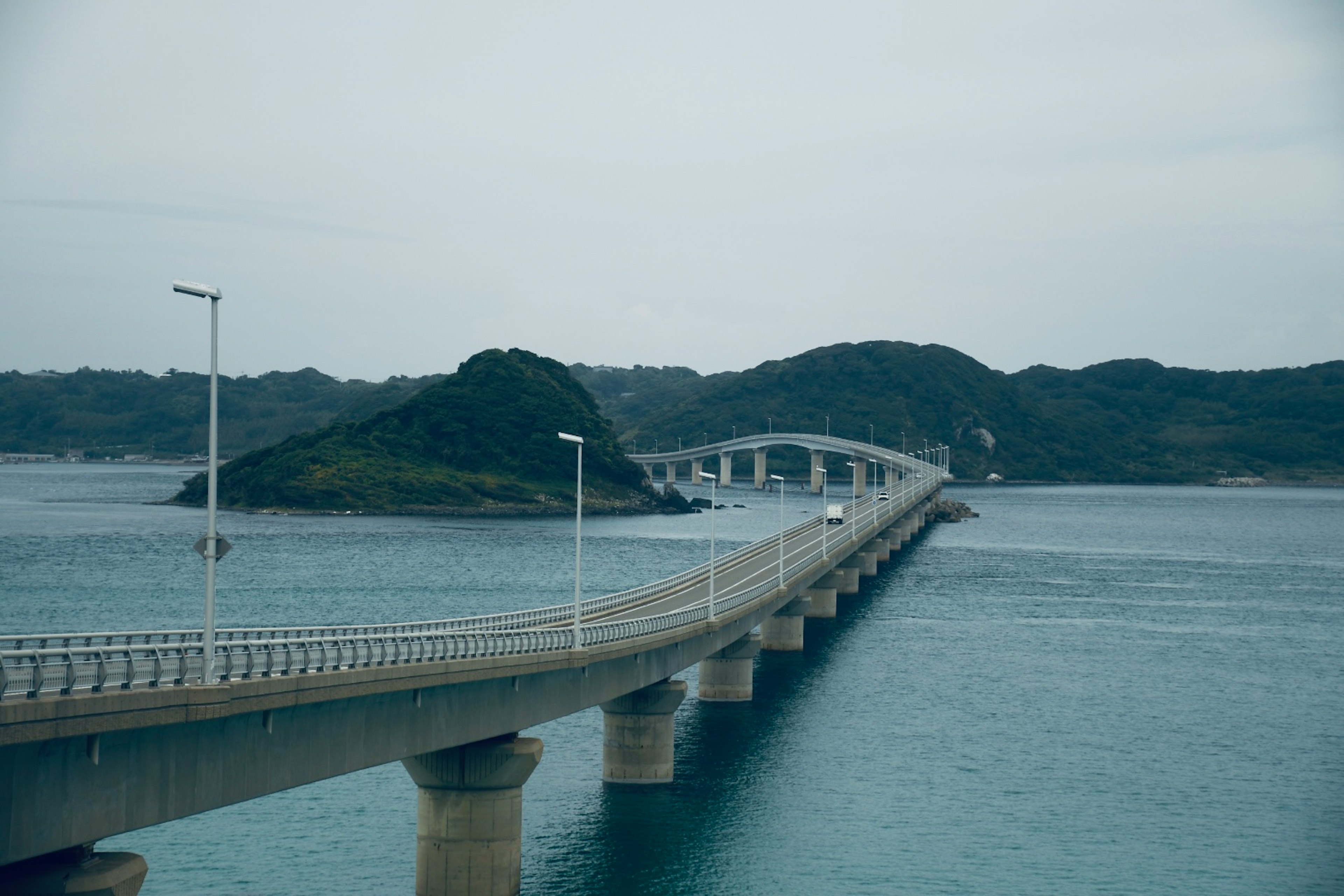 A long bridge spanning over the sea with surrounding green islands