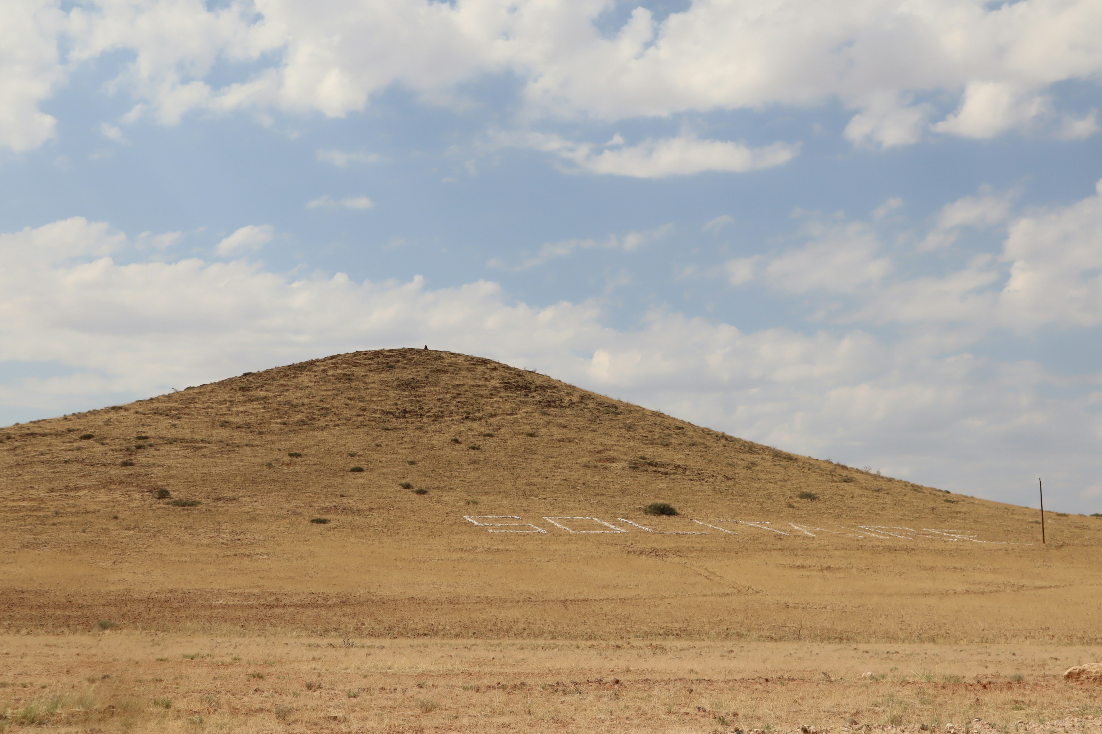 Una piccola collina in una prateria secca con cielo nuvoloso