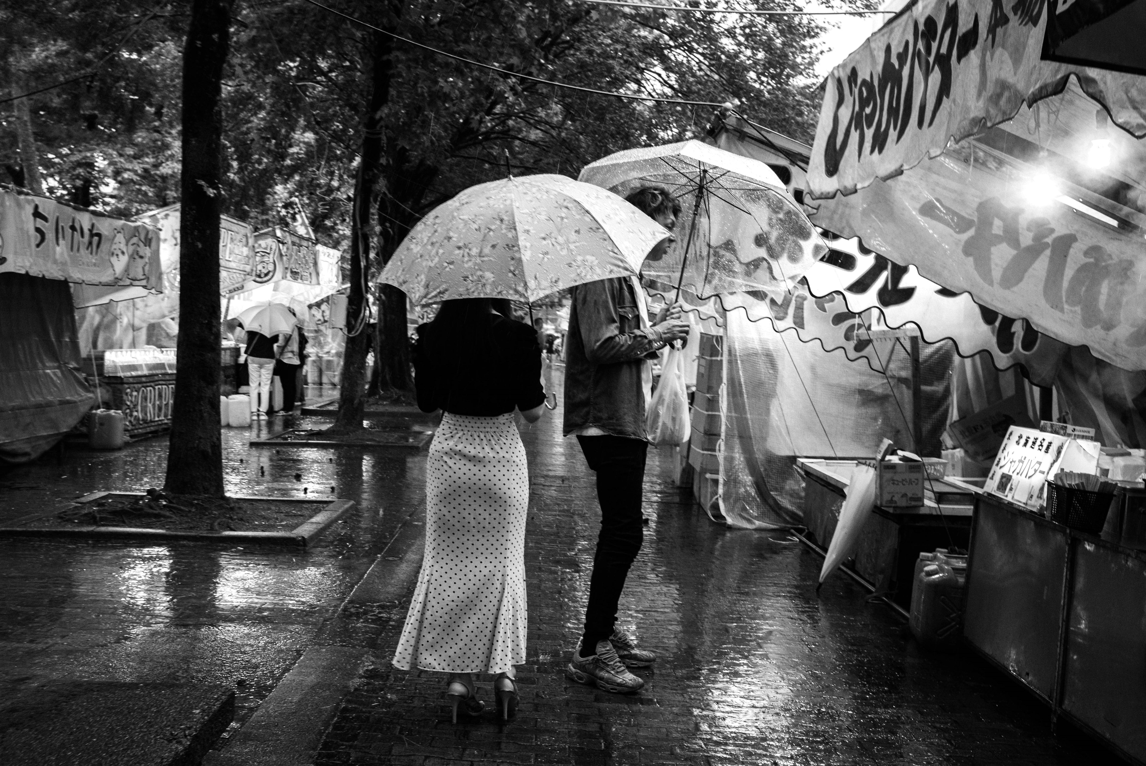 雨の中、傘を持つ二人の人物が並んでいる白黒のストリートシーン