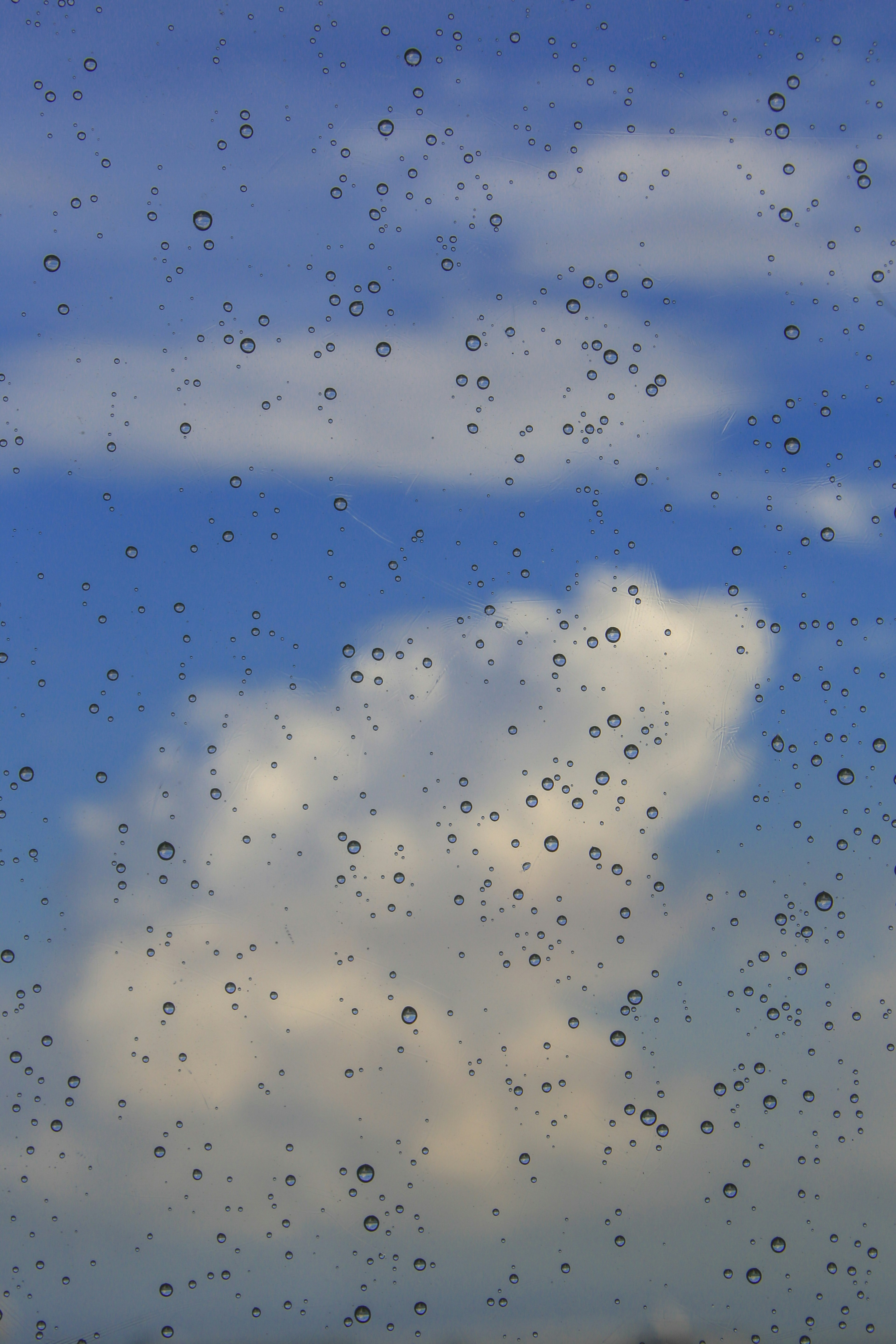 Vista del cielo azul y las nubes a través de una ventana salpicada de lluvia