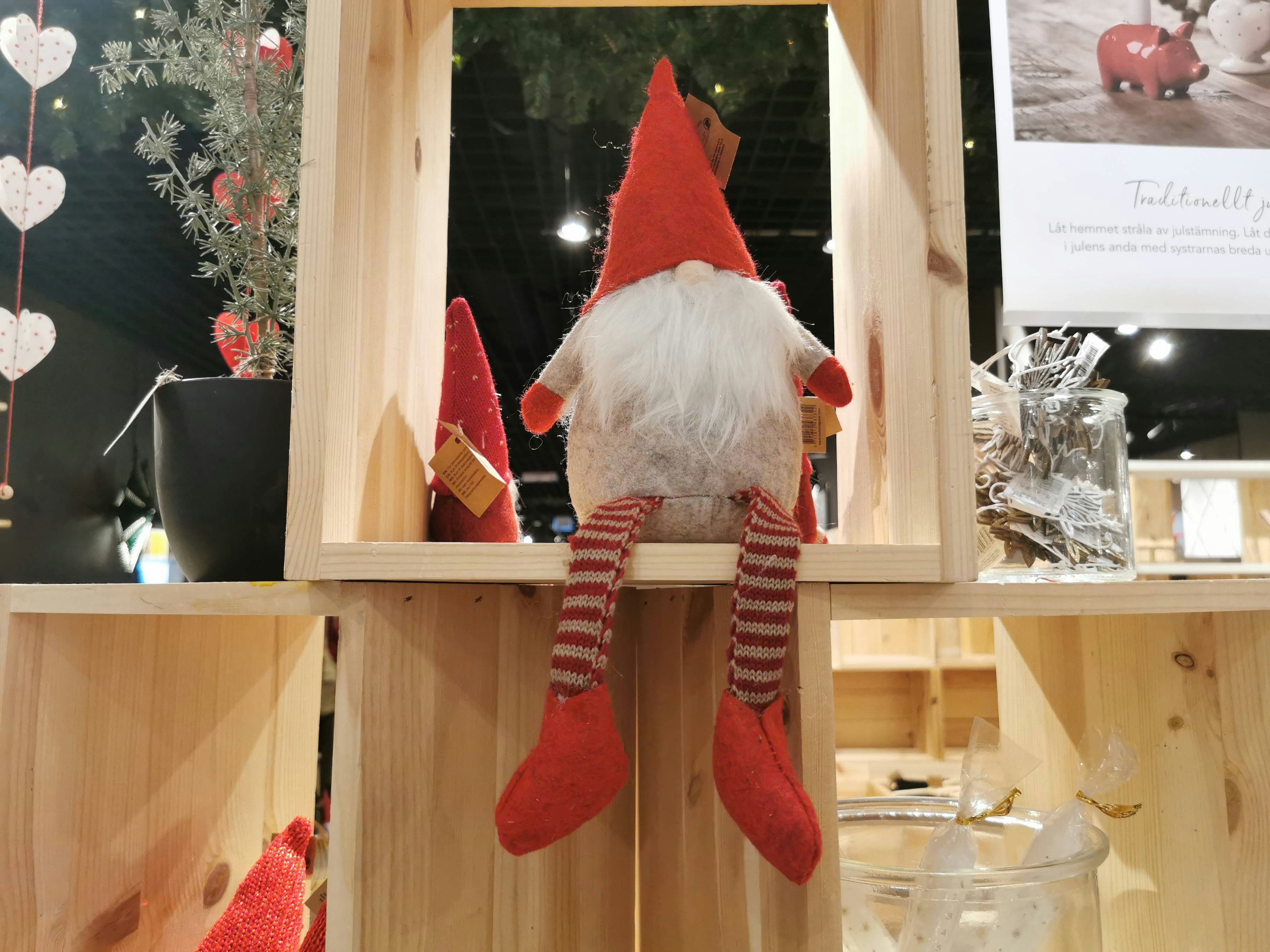 Un petit gnome avec un chapeau rouge et des chaussettes rayées assis sur une étagère en bois