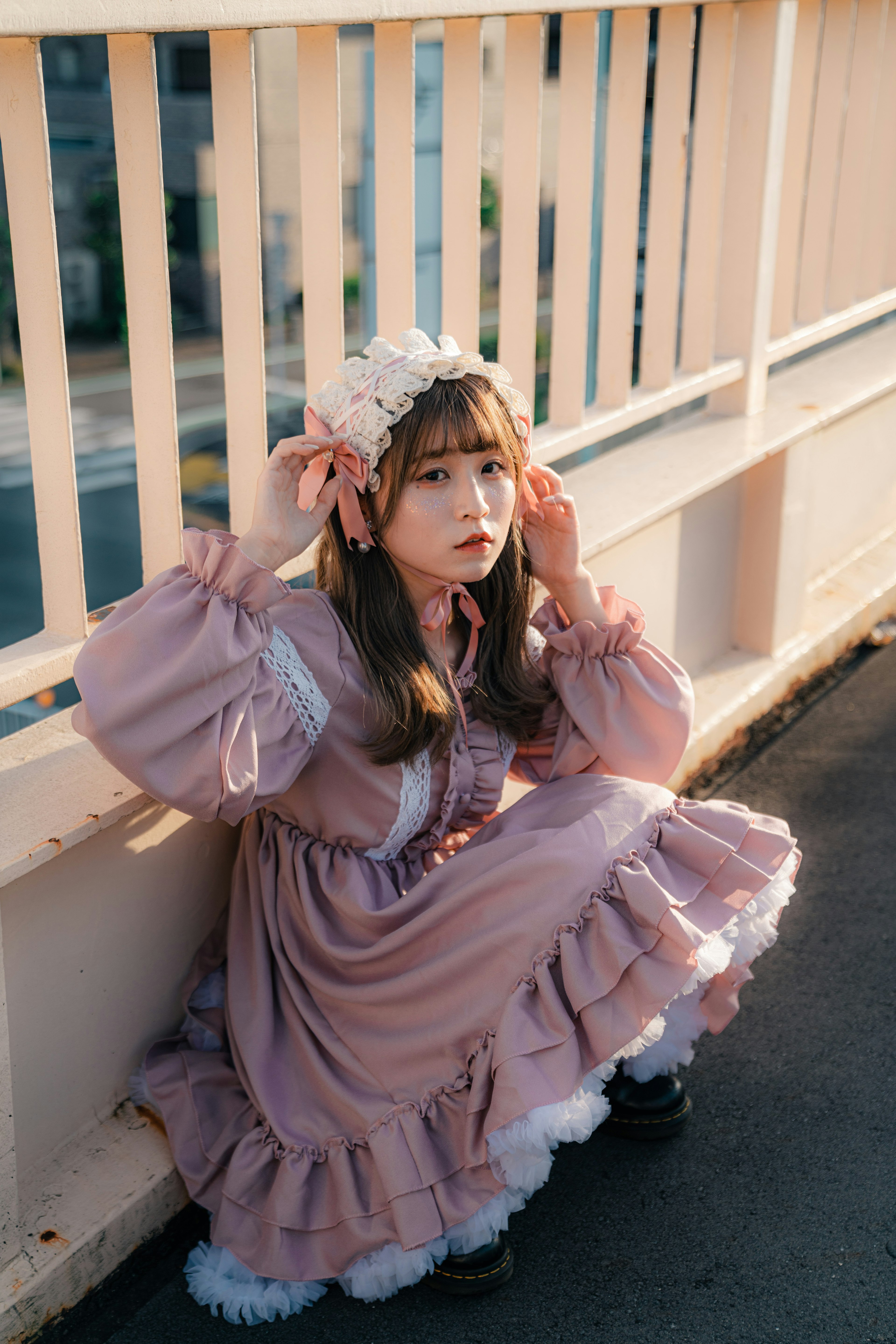 A girl wearing a pink dress with a floral hair accessory sitting against a railing