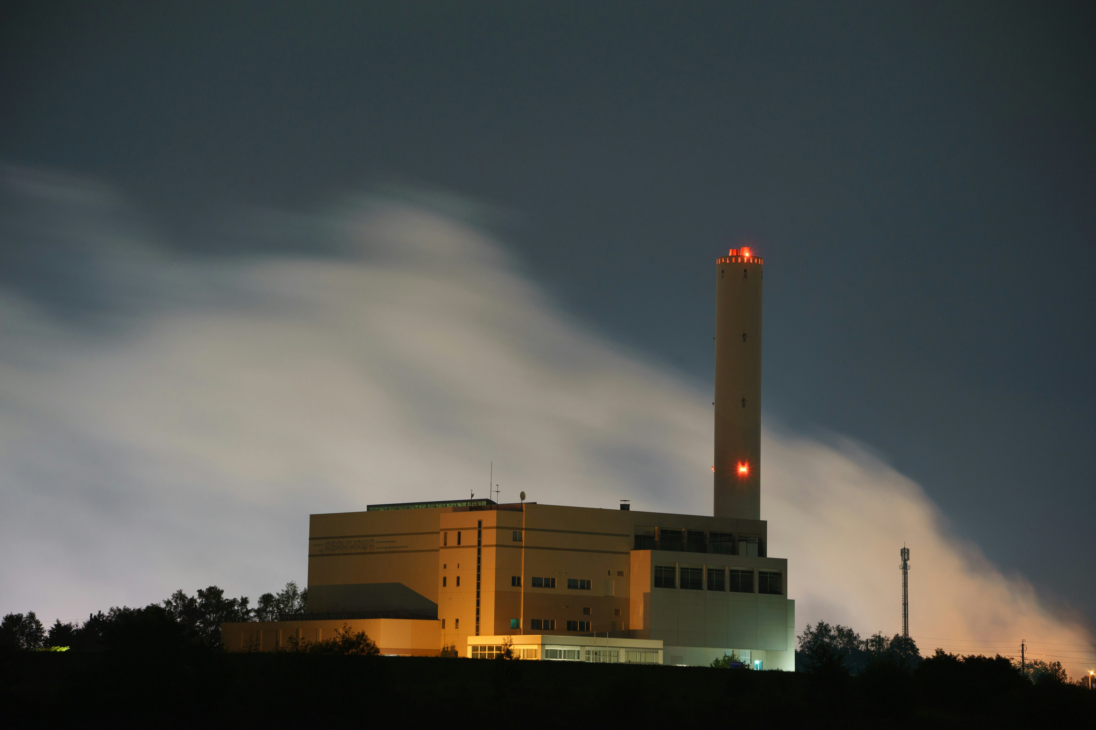 Image nocturne d'une usine avec une cheminée éclairée et des nuages