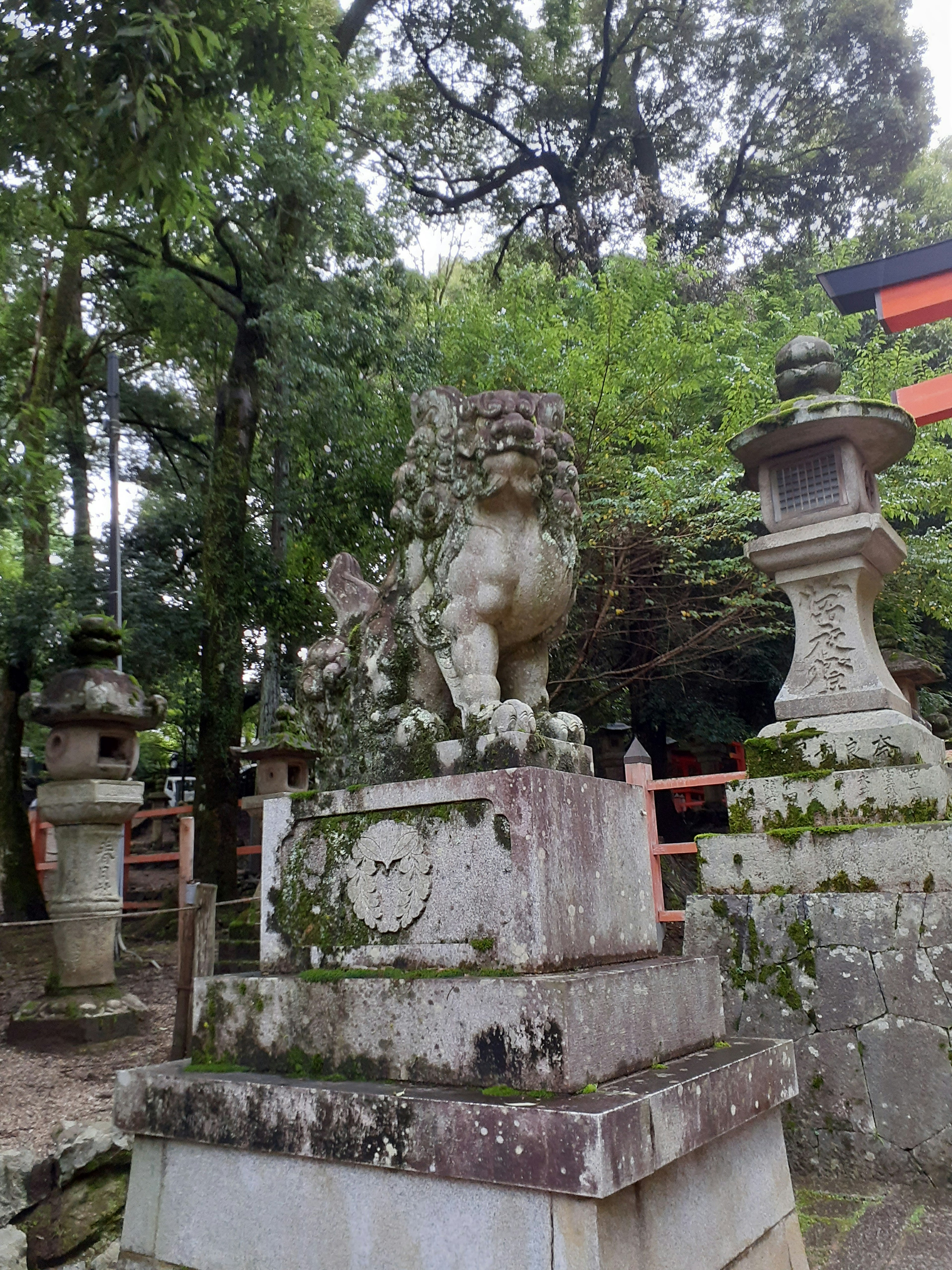 Statue de lion en pierre sur un piédestal couvert de mousse entourée de verdure luxuriante