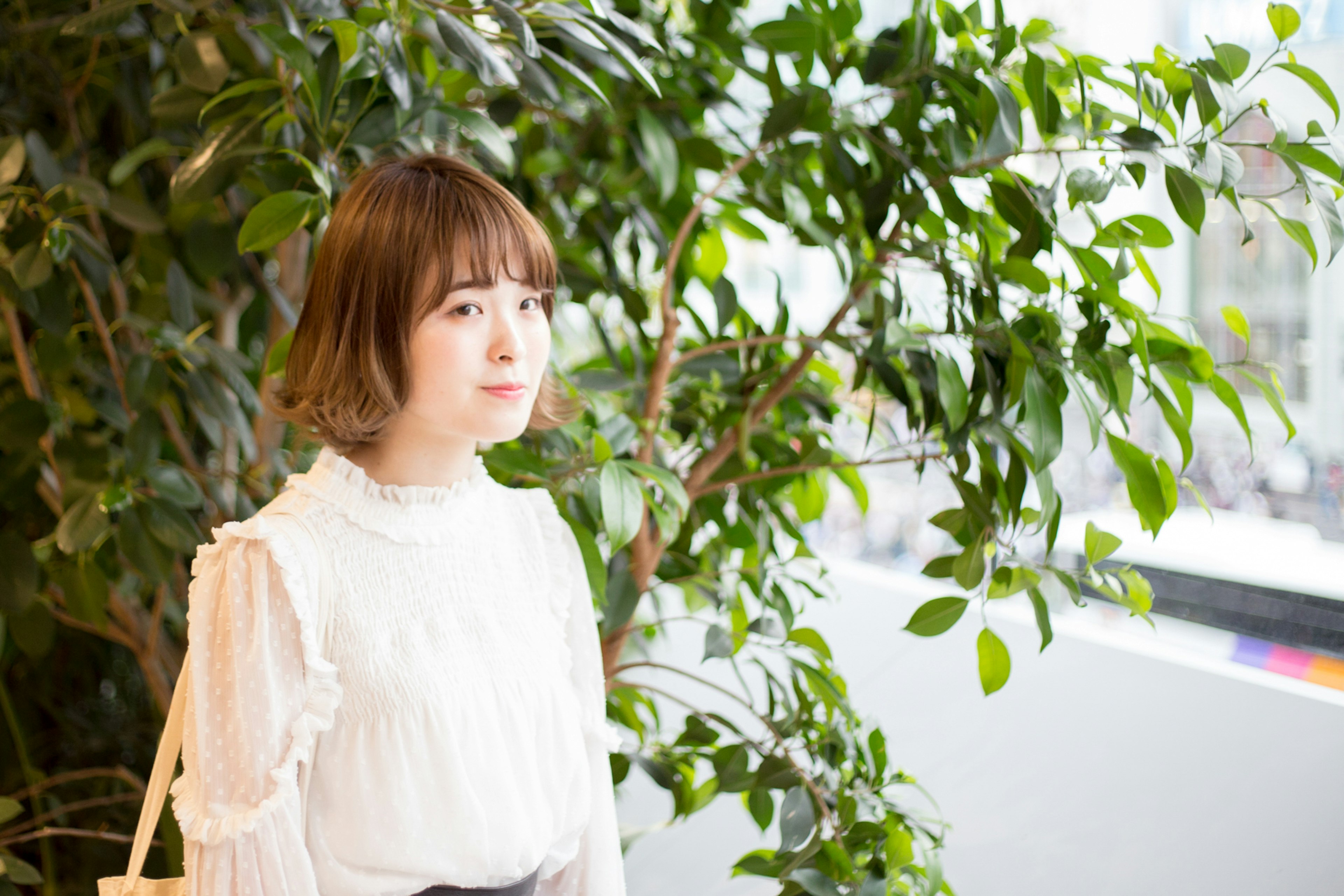 Una mujer con blusa blanca de pie frente a plantas verdes