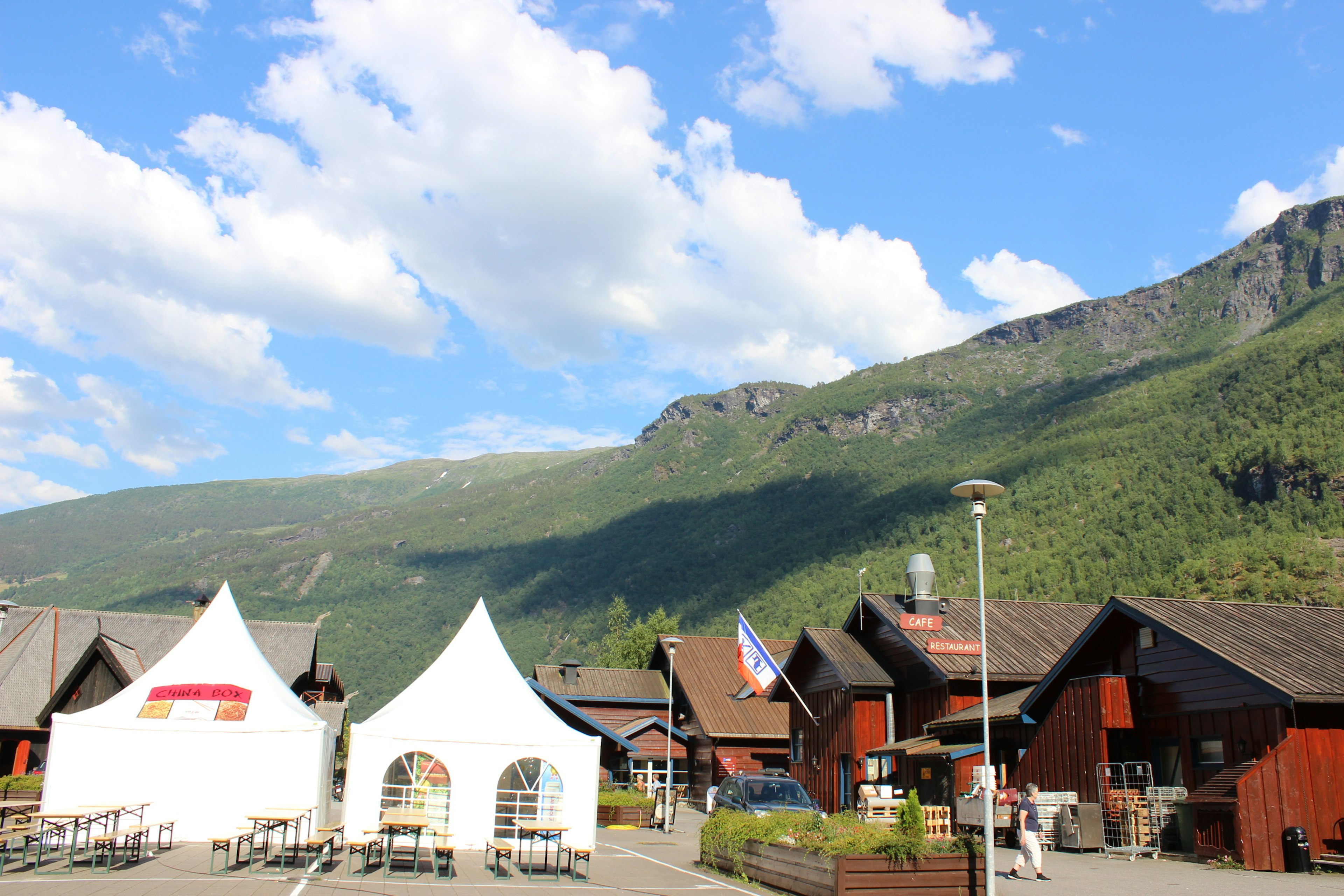 Malereiansicht eines norwegischen Dorfes mit Bergen im Hintergrund weiße Zelte und Holzhäuser in einer üppigen grünen Umgebung