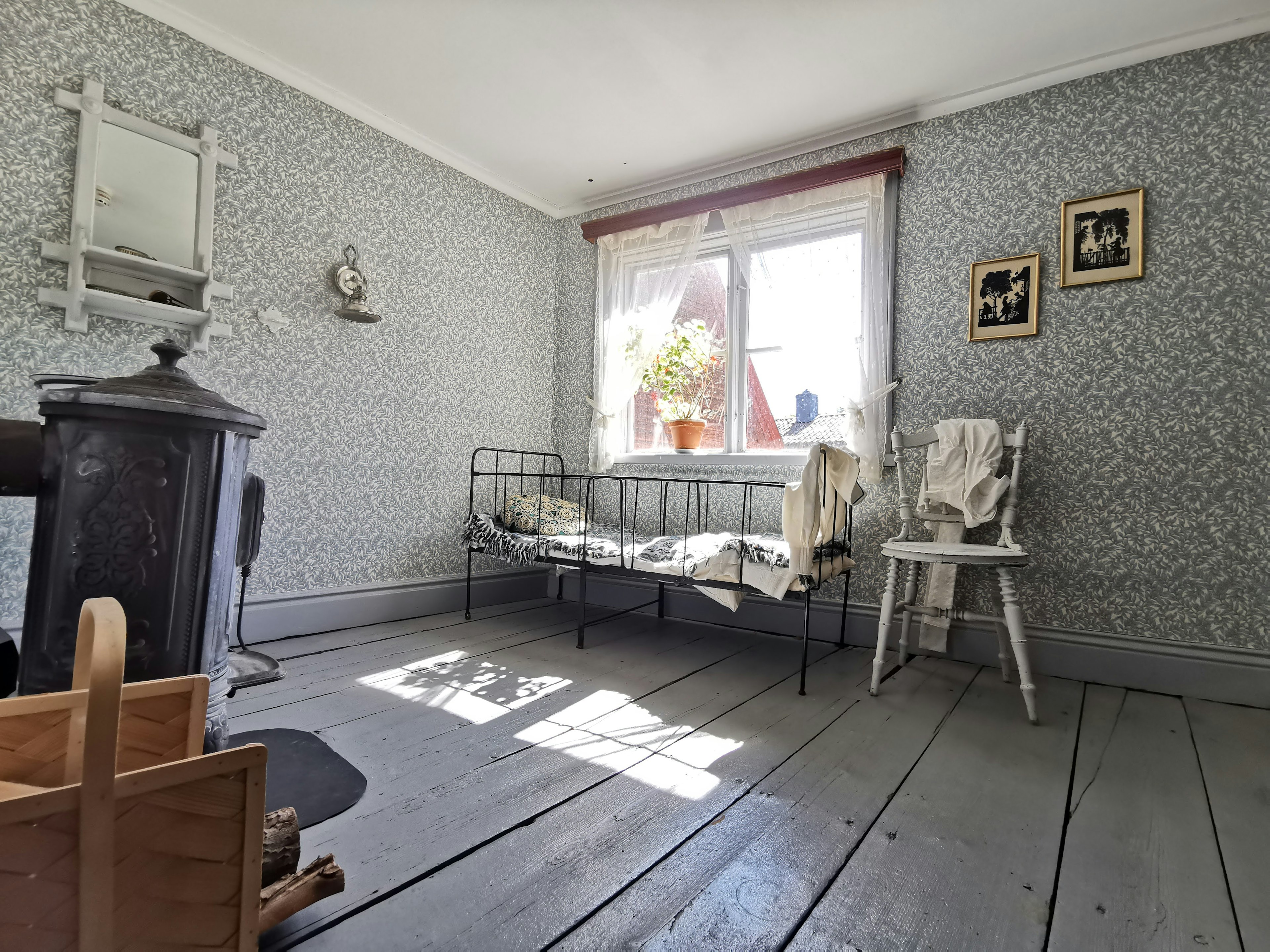 Habitación luminosa con luz solar que entra por una ventana decorada con flores cama antigua y silla dispuestas en el interior