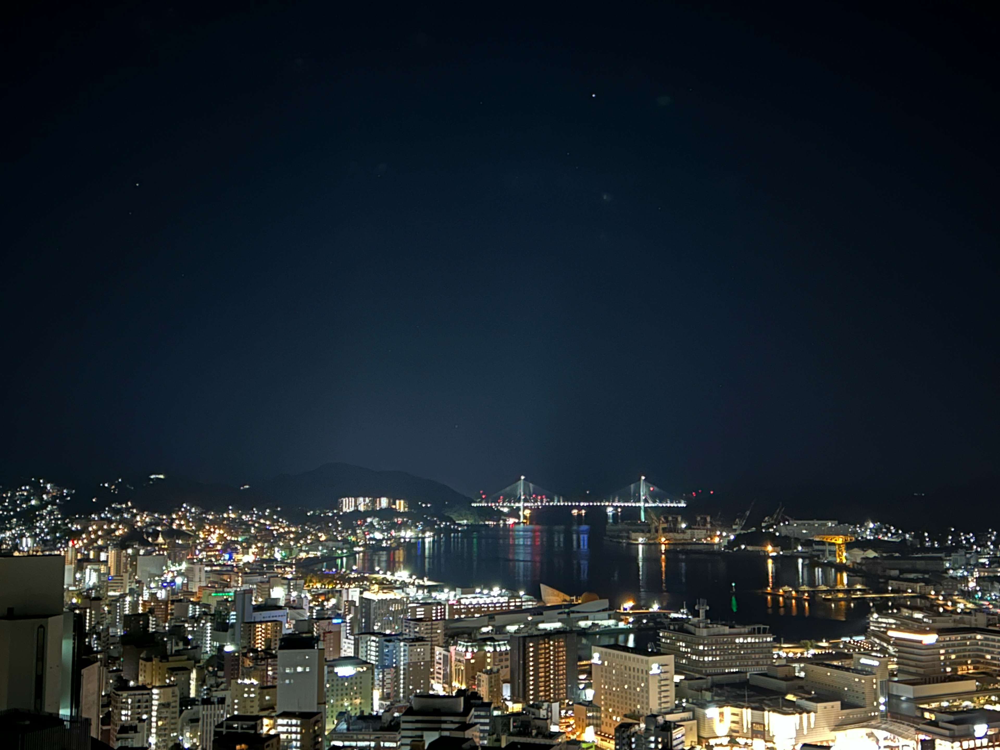 Night view of a cityscape with shimmering lights and a bay illuminated by buildings