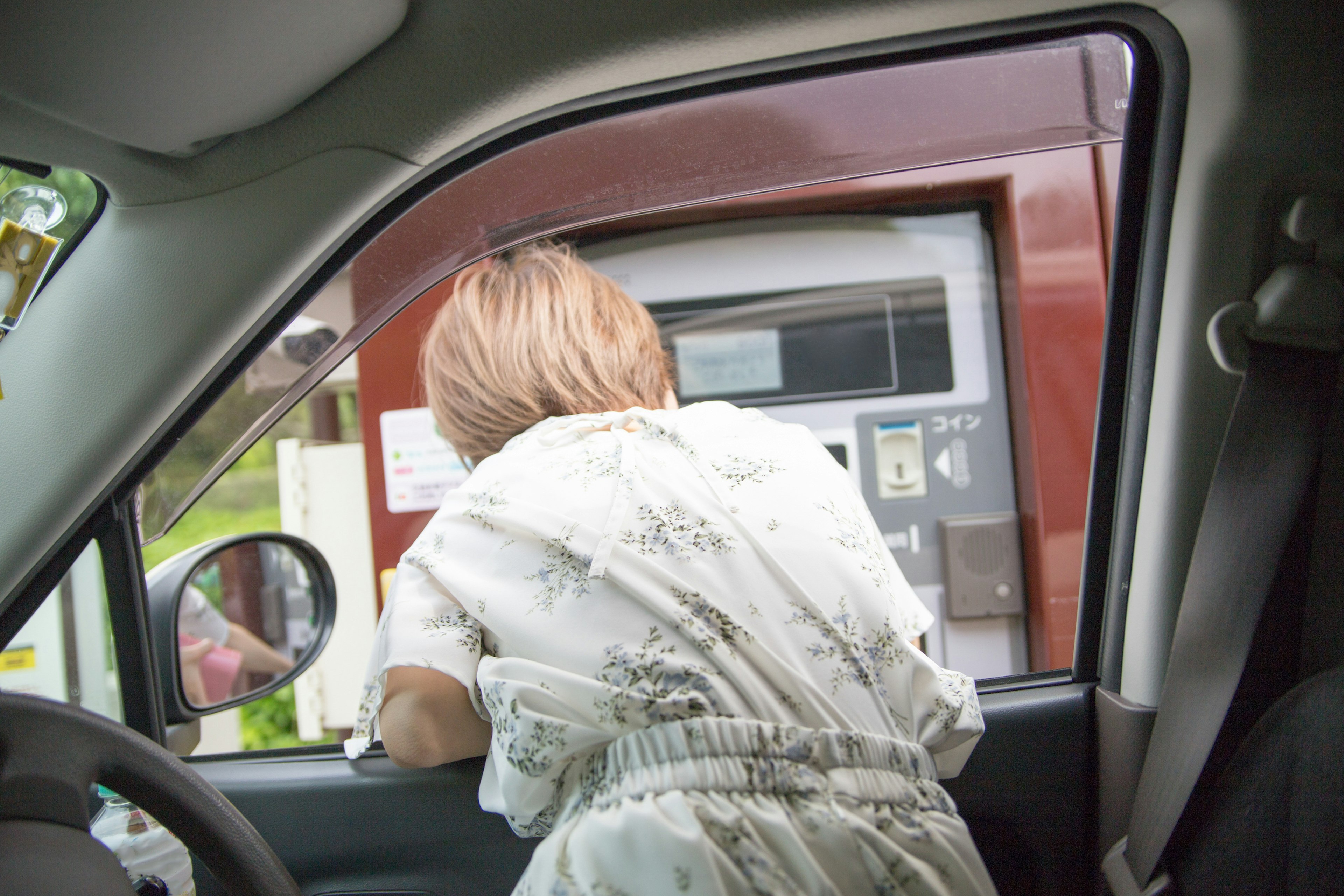 Une femme se penchant par la fenêtre d'une voiture pour utiliser un distributeur automatique