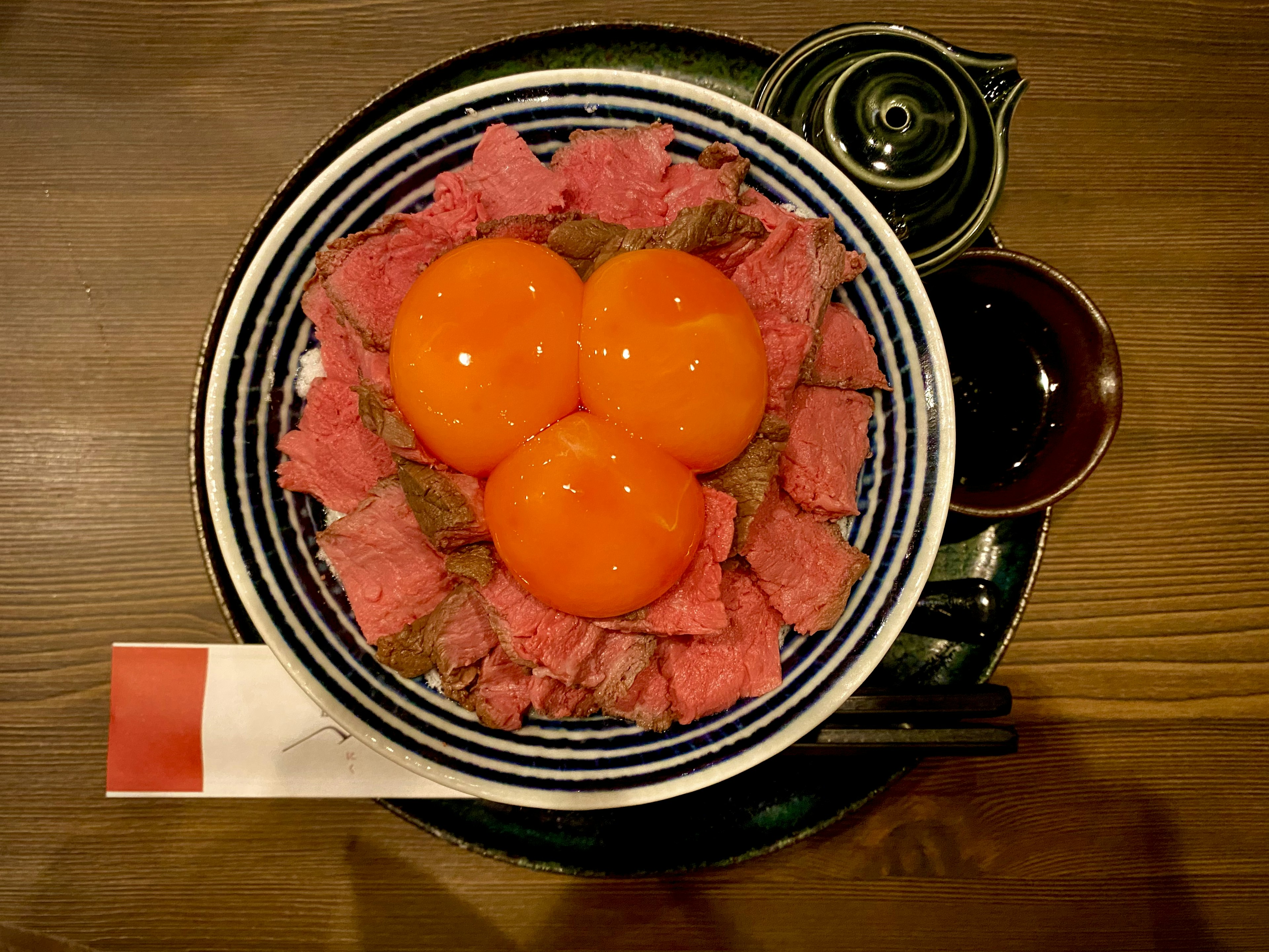 赤い卵黄と薄切りの肉が盛られた丼