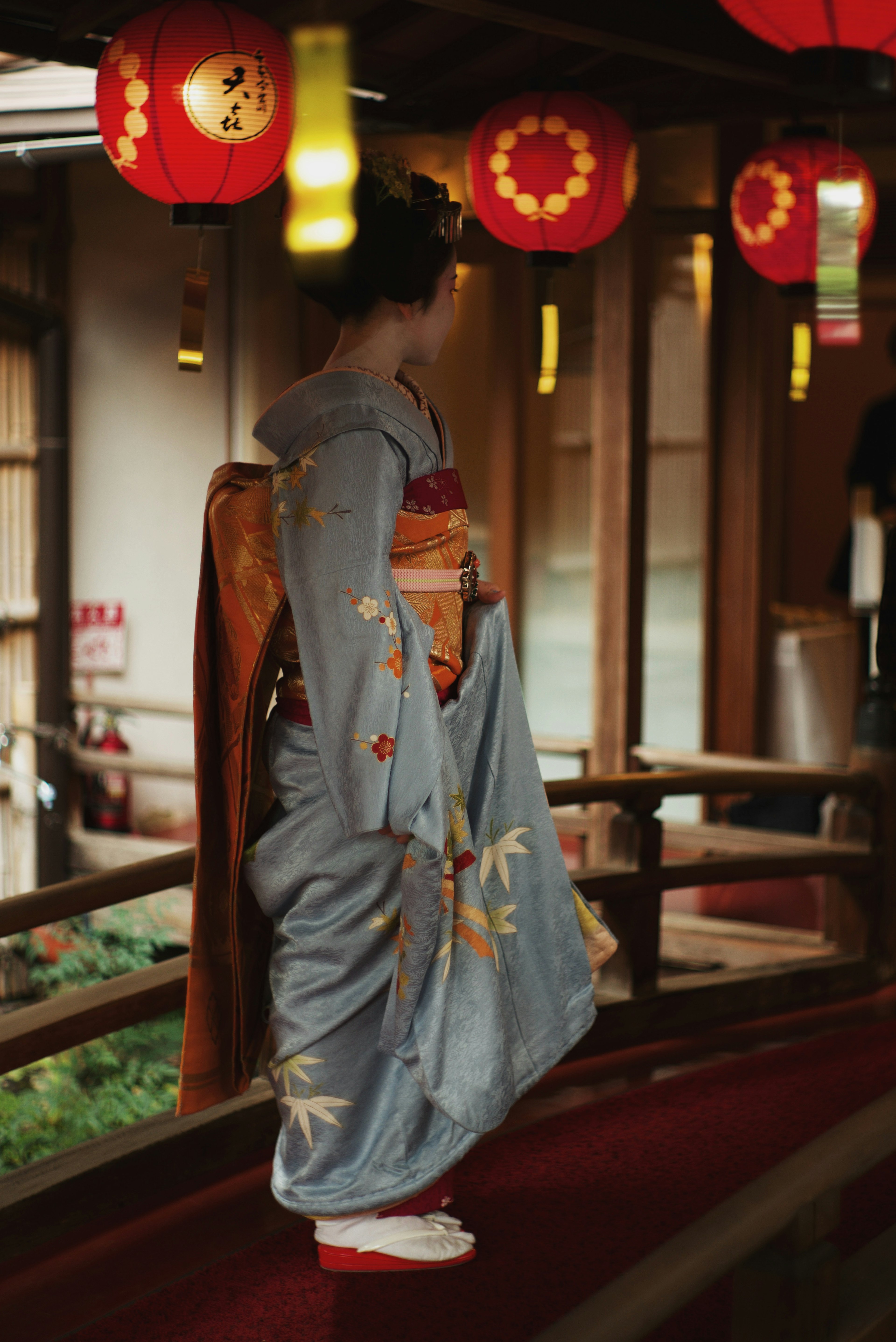 Une femme en kimono bleu marchant dans un bâtiment japonais traditionnel avec des lanternes rouges