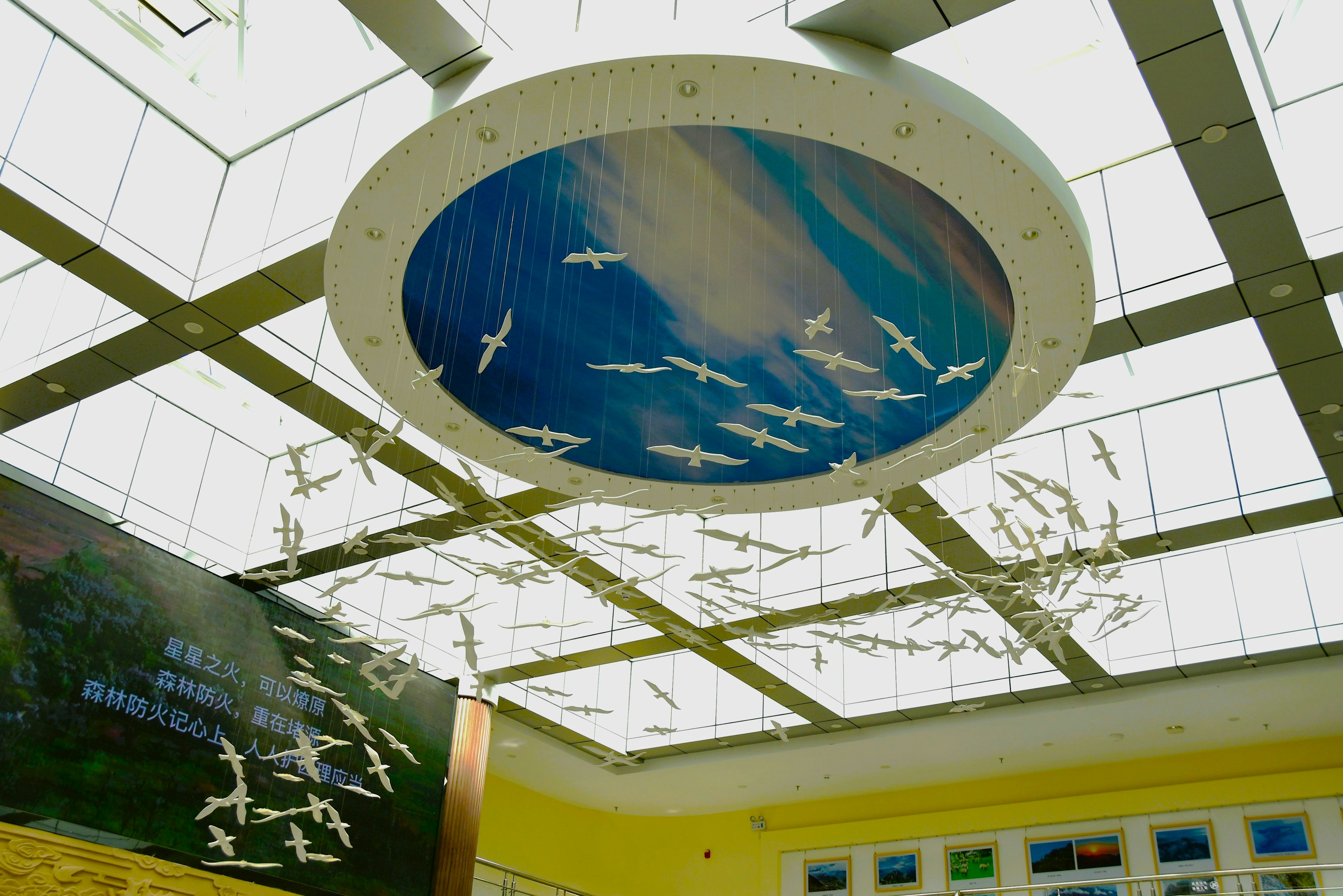 Una instalación en el techo con esculturas de aves blancas y un mural de cielo azul