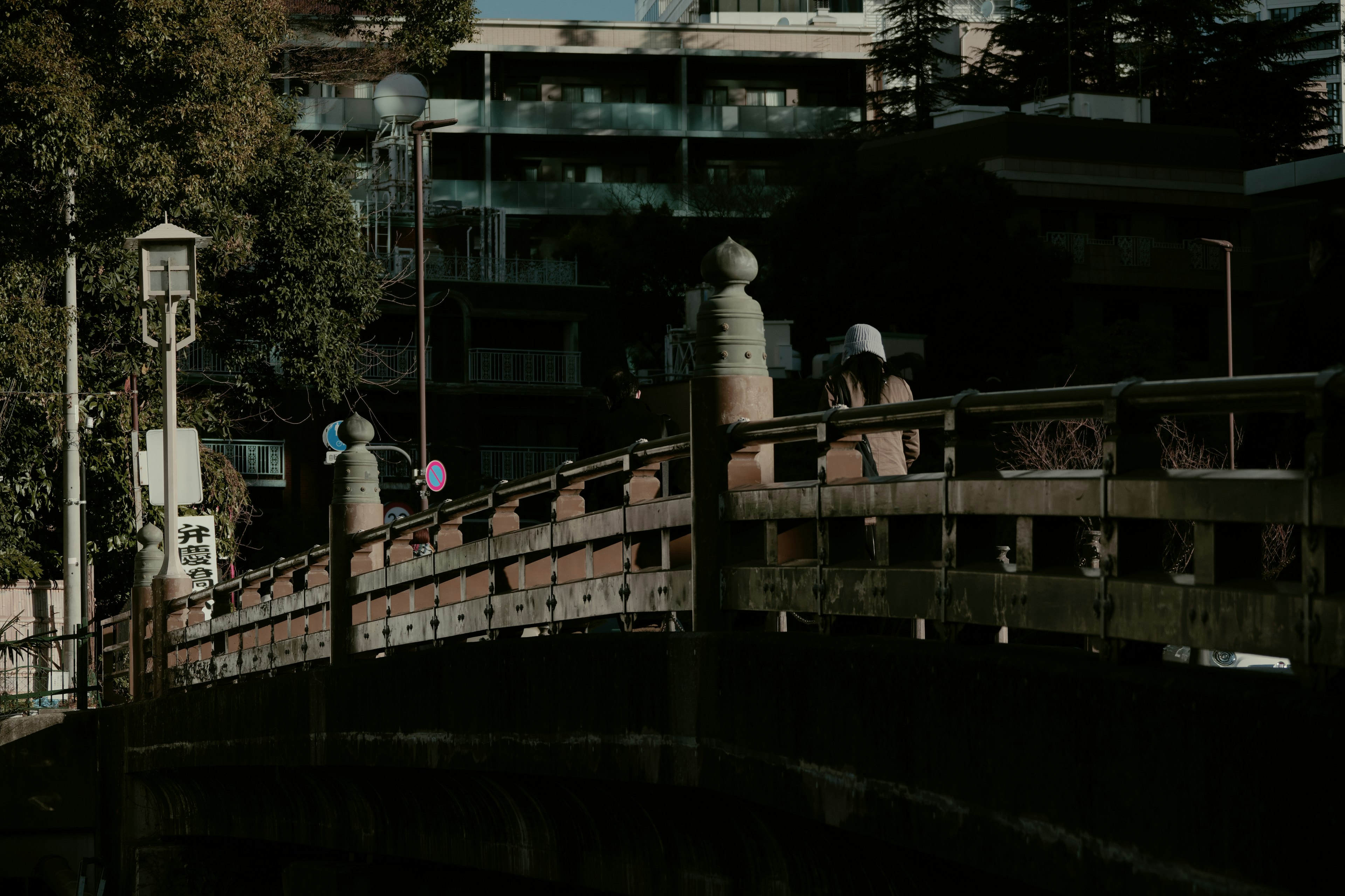 A bridge with people walking and nearby buildings in a dimly lit scene