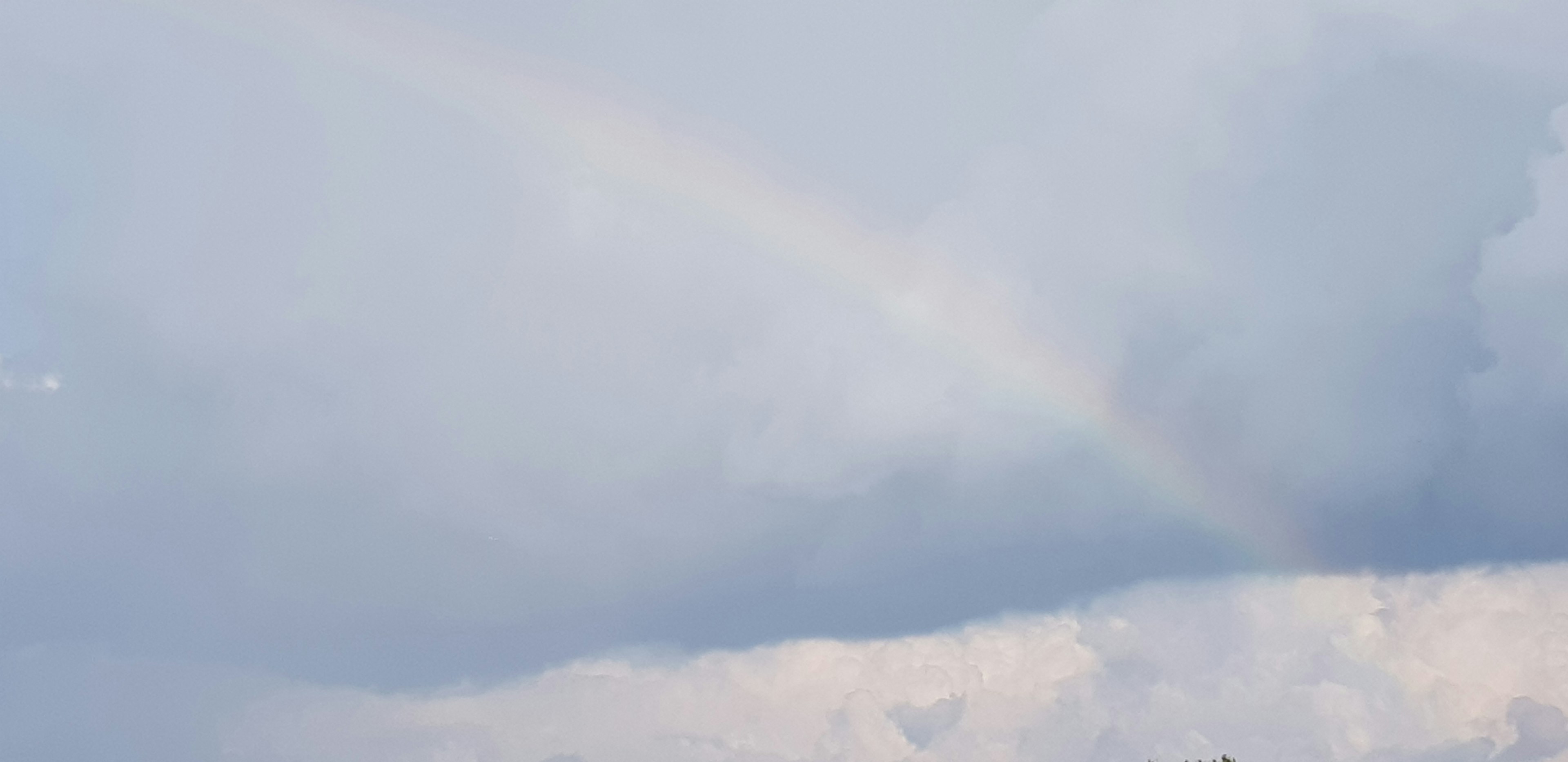 Un leggero arcobaleno che si erge in un cielo blu chiaro con nuvole