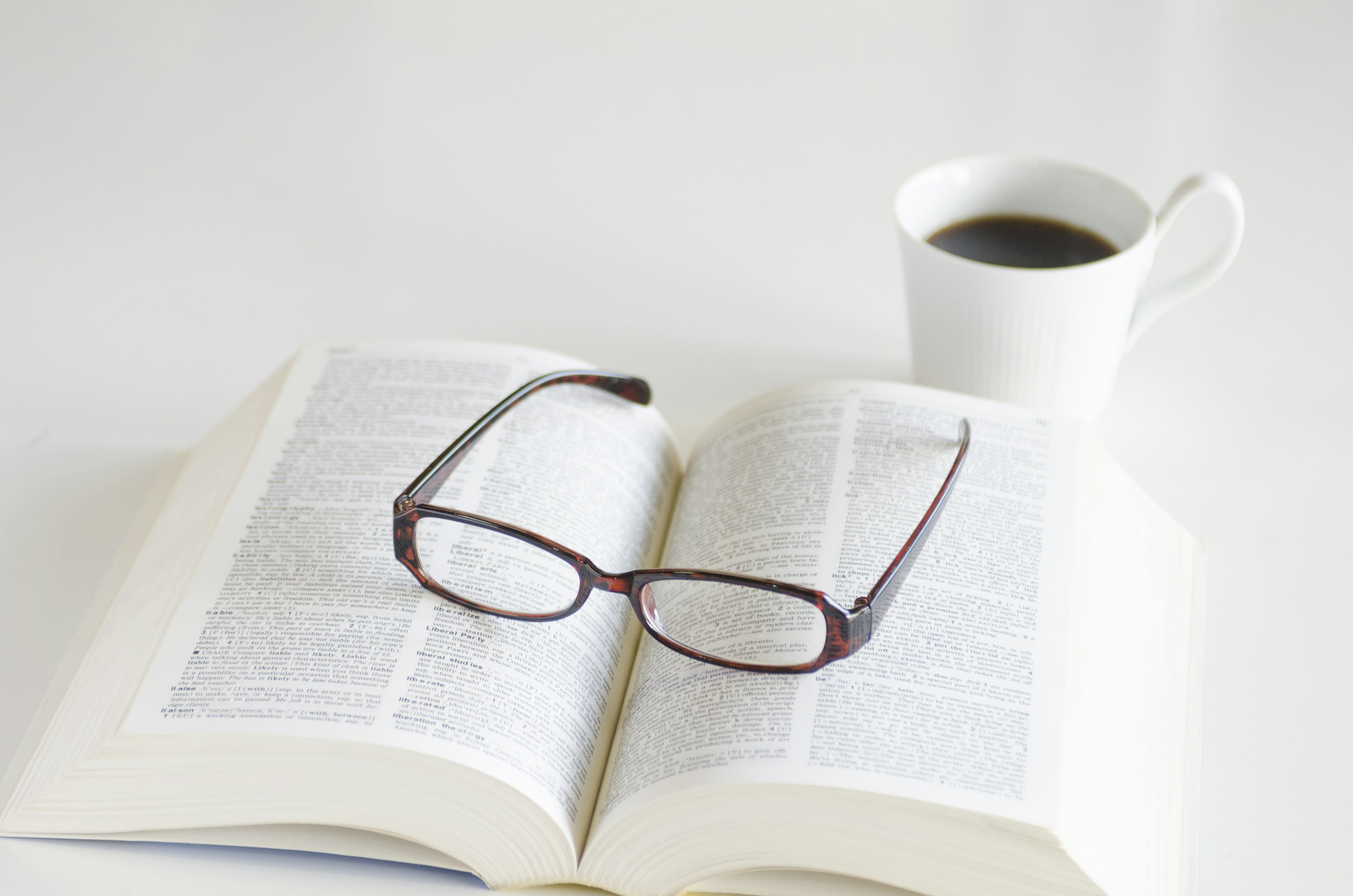 Lunettes posées sur un livre ouvert avec une tasse de café à proximité