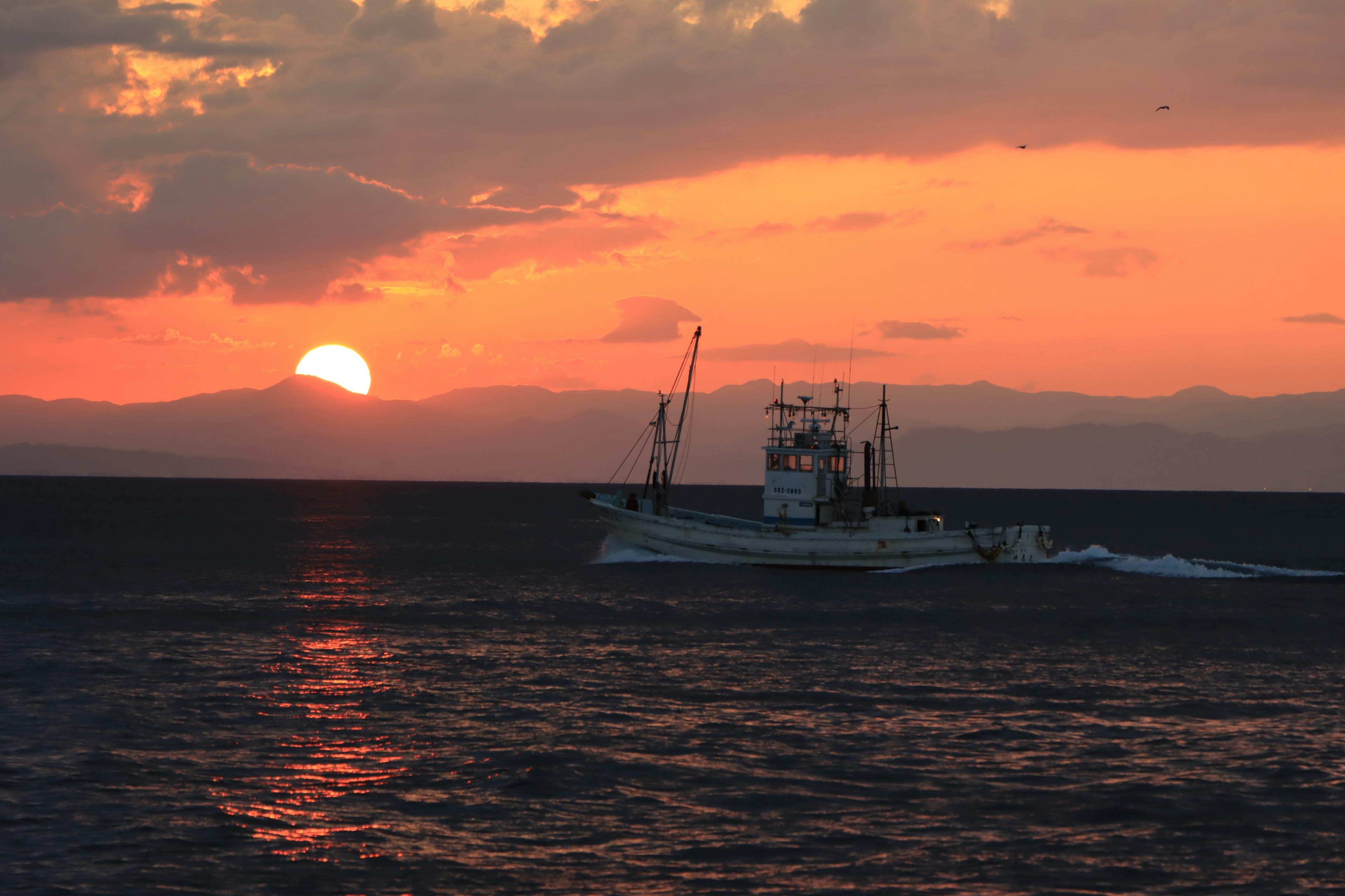 Bateau de pêche naviguant sur la mer au coucher du soleil avec des couleurs vibrantes