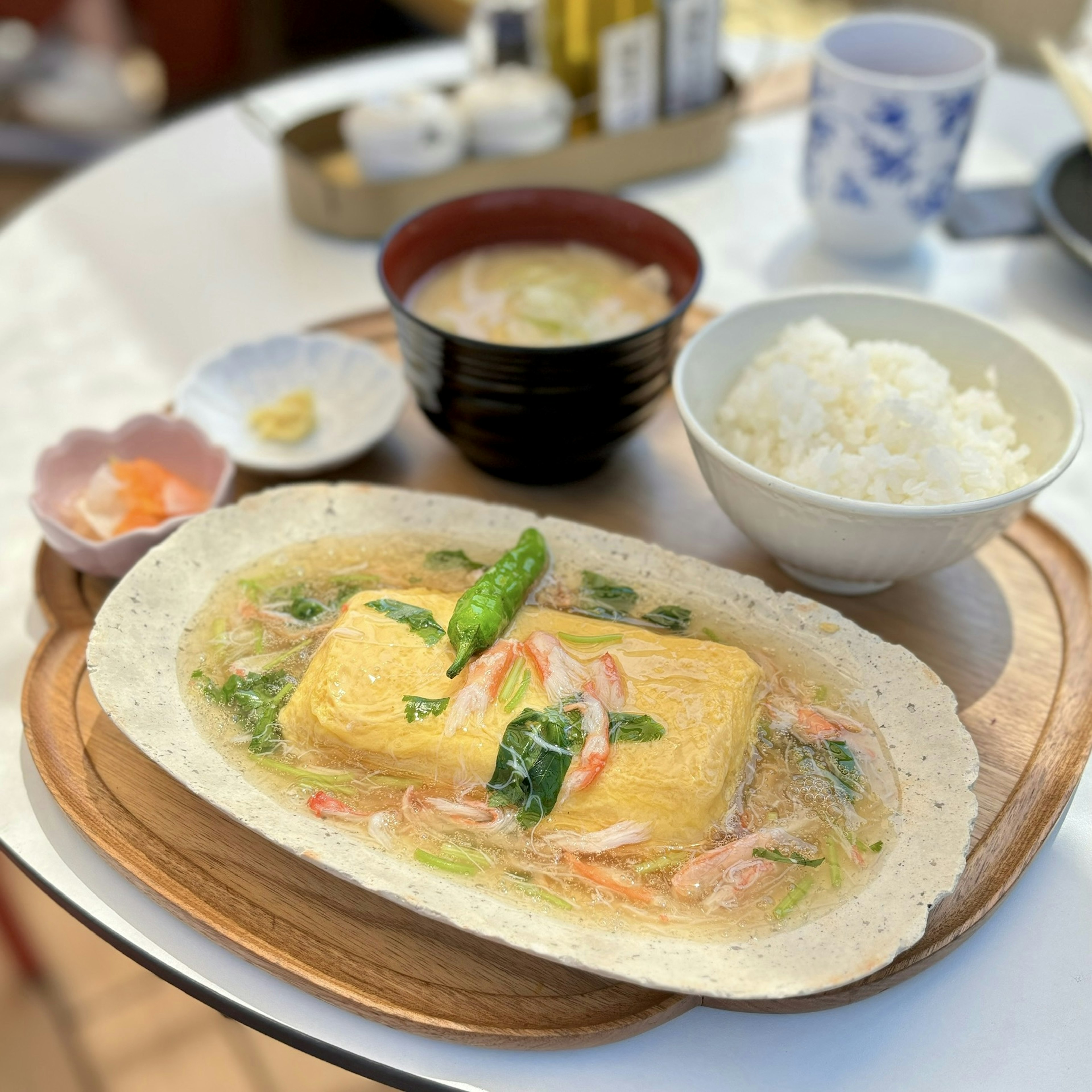 温かい卵豆腐の料理が盛り付けられた木の皿の上にありアスパラガスと野菜がトッピングされている