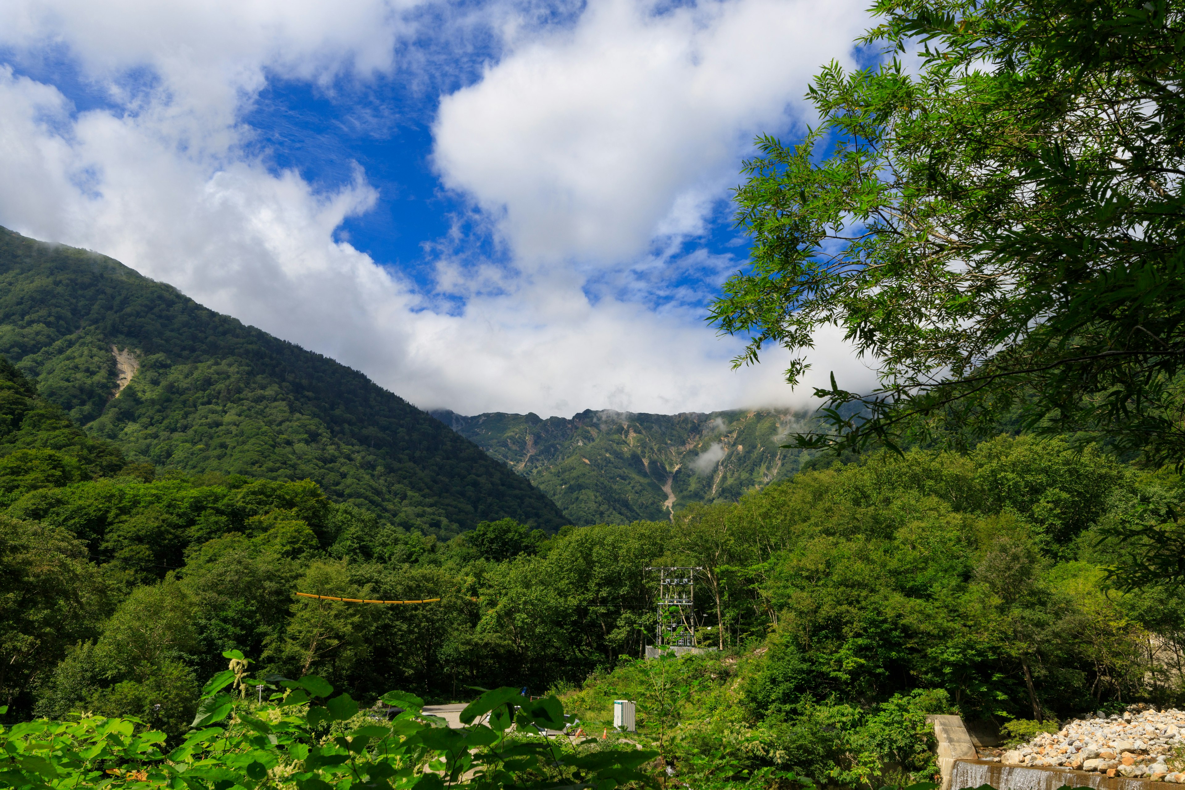 Montagnes verdoyantes sous un ciel bleu avec des nuages couvrant les sommets