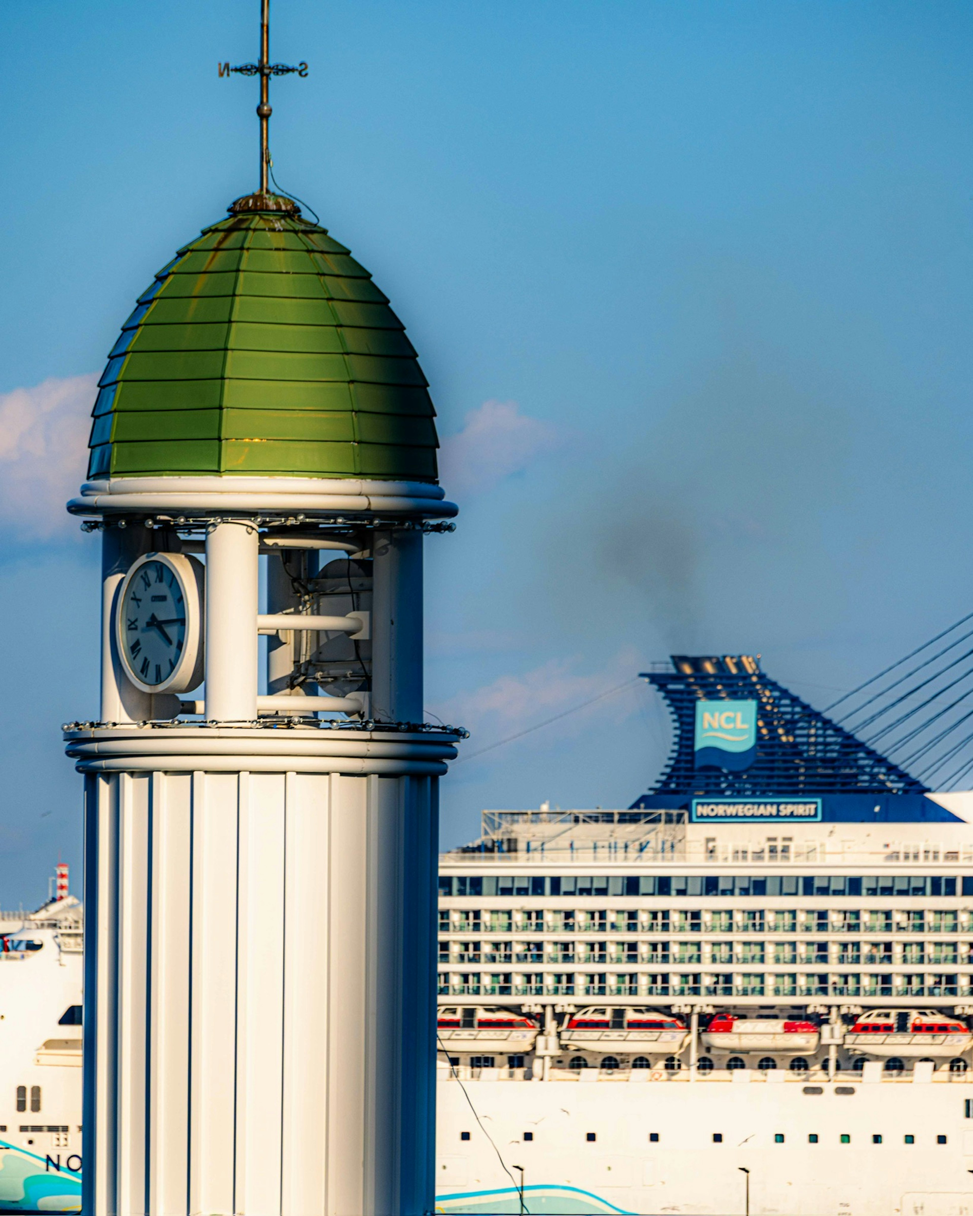 Clock tower with a green dome and a large cruise ship in the background