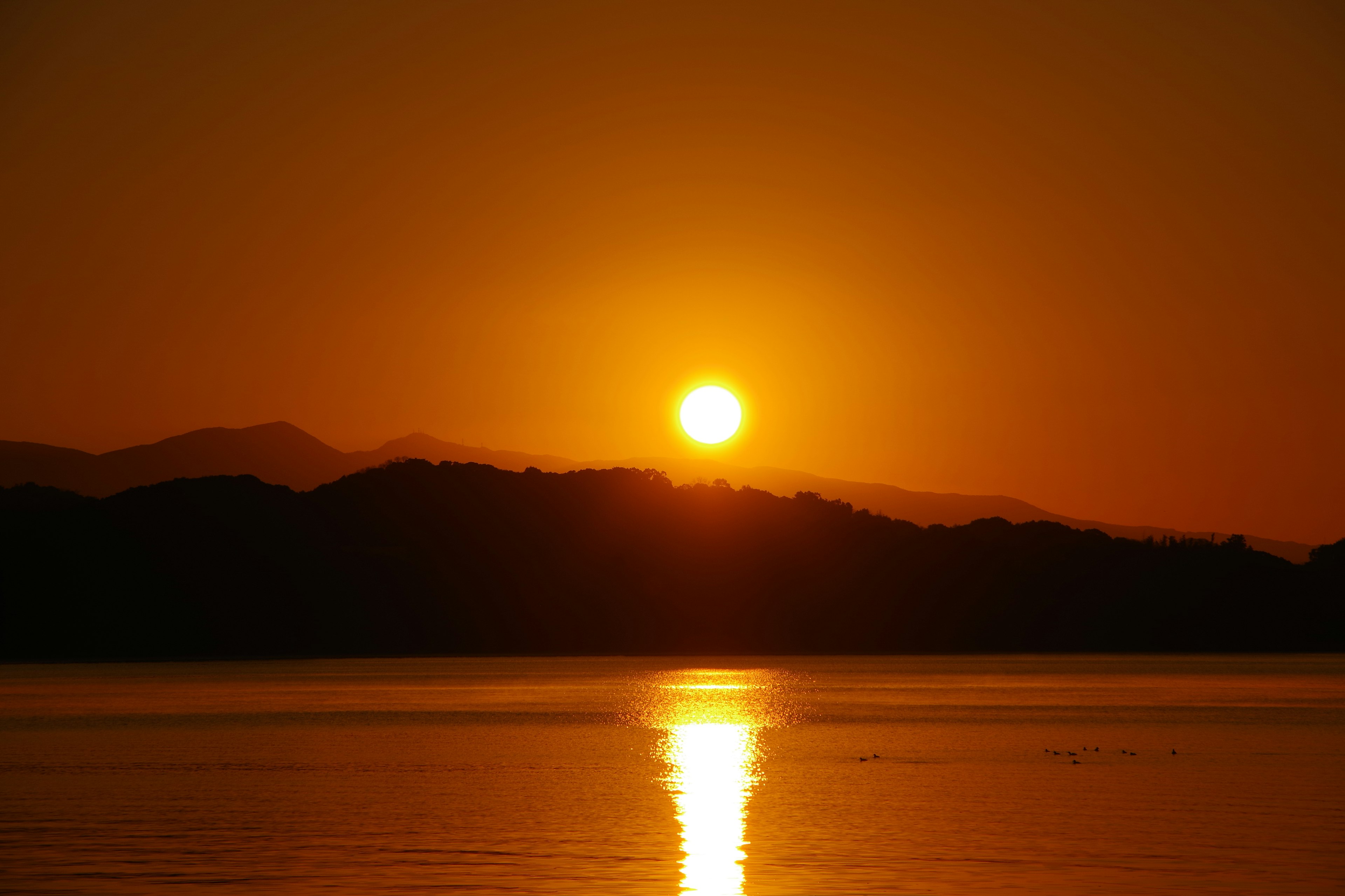 Ein schöner Sonnenuntergang mit einer orangefarbenen Sonne, die hinter silhouettierten Bergen untergeht