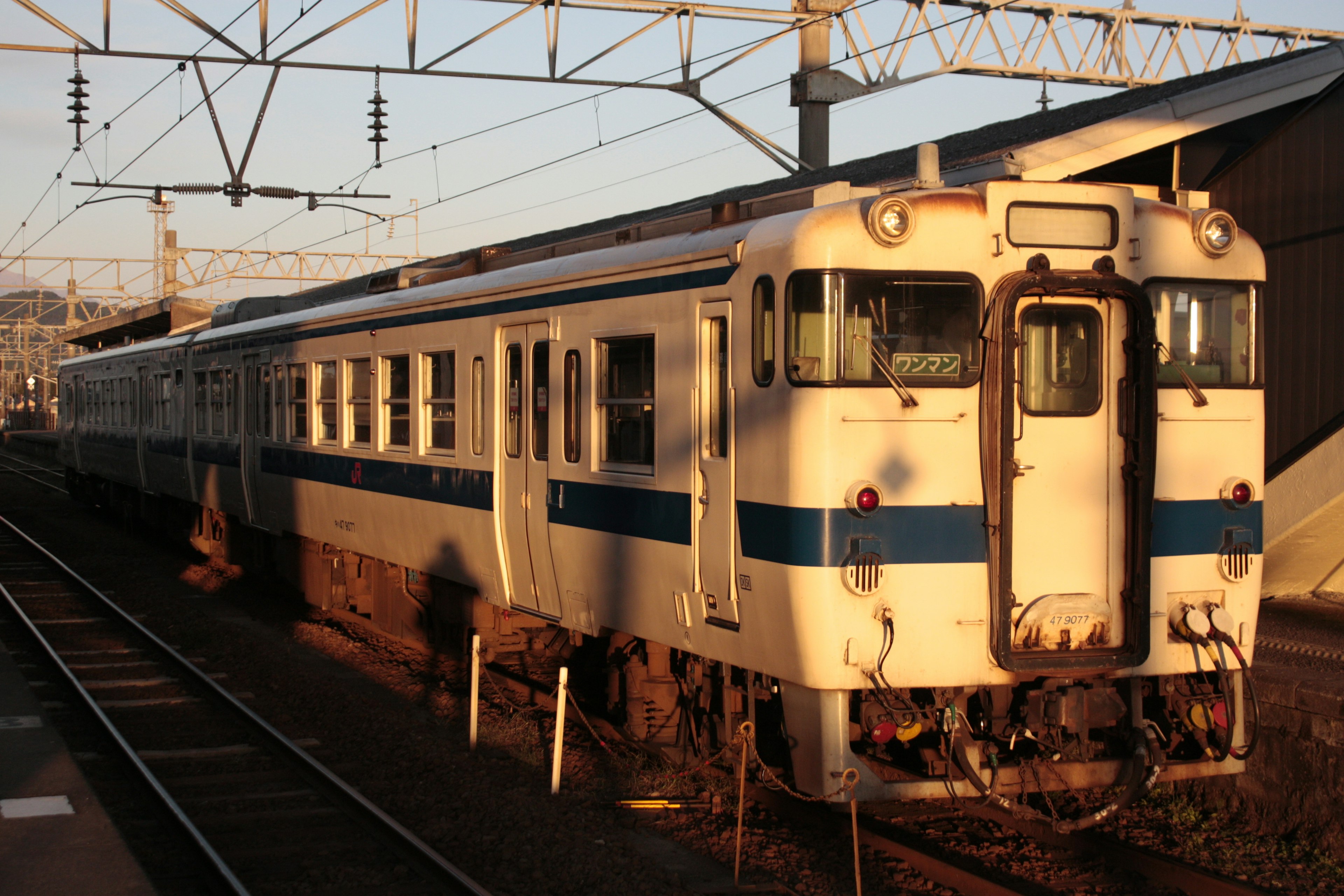 A white and blue train parked at the station under the sunset