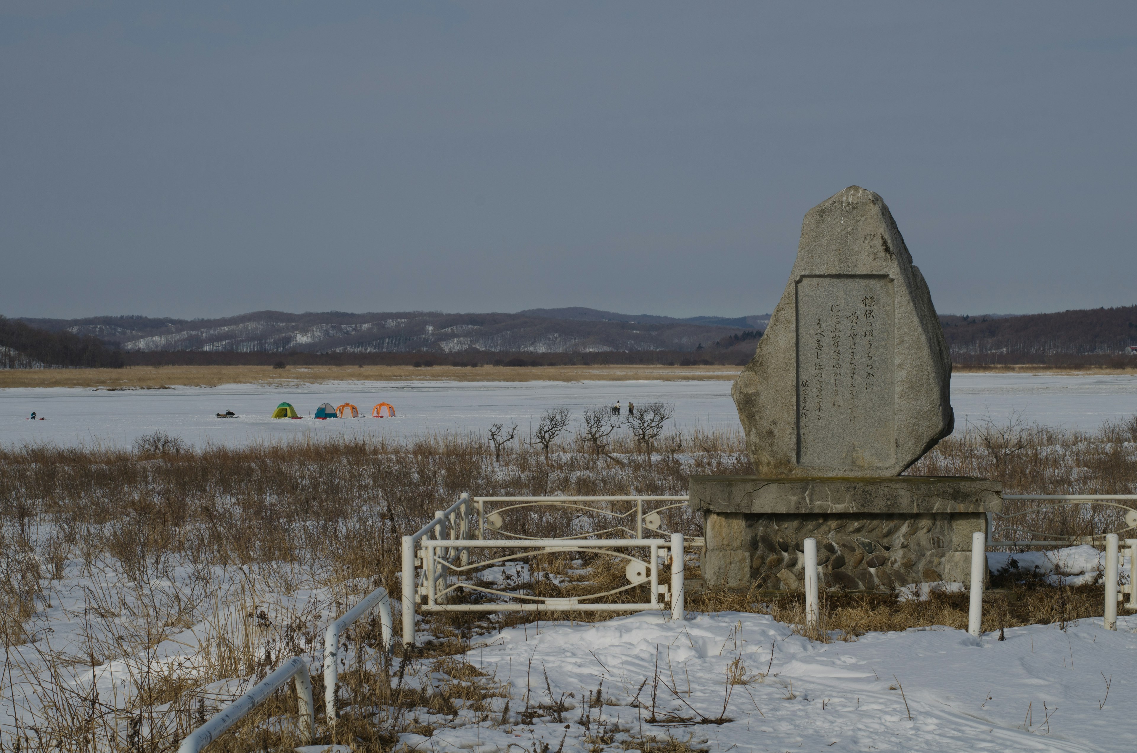 A stone monument in a snowy landscape with tents visible in the distance