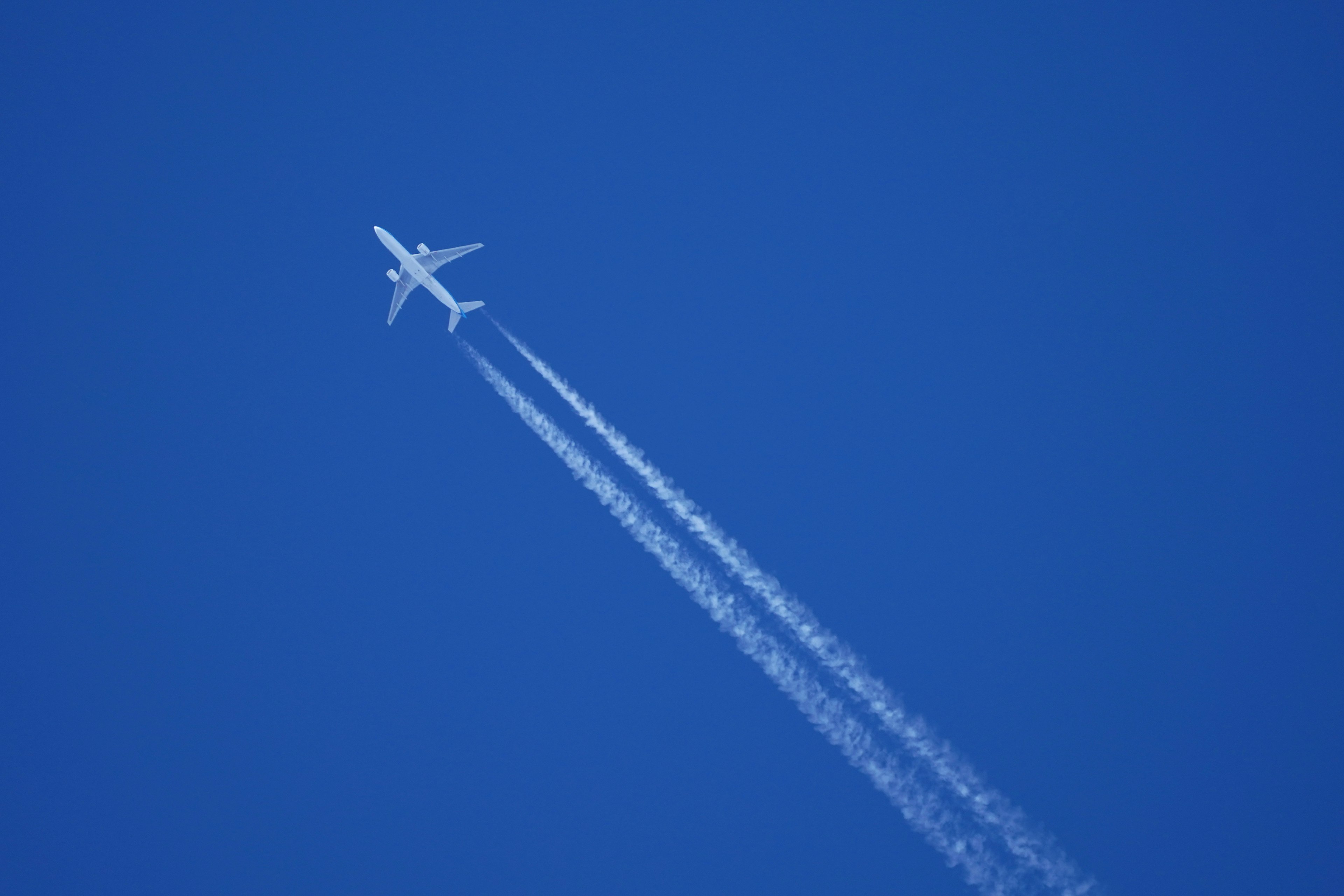 An airplane ascending against a blue sky with contrails trailing behind