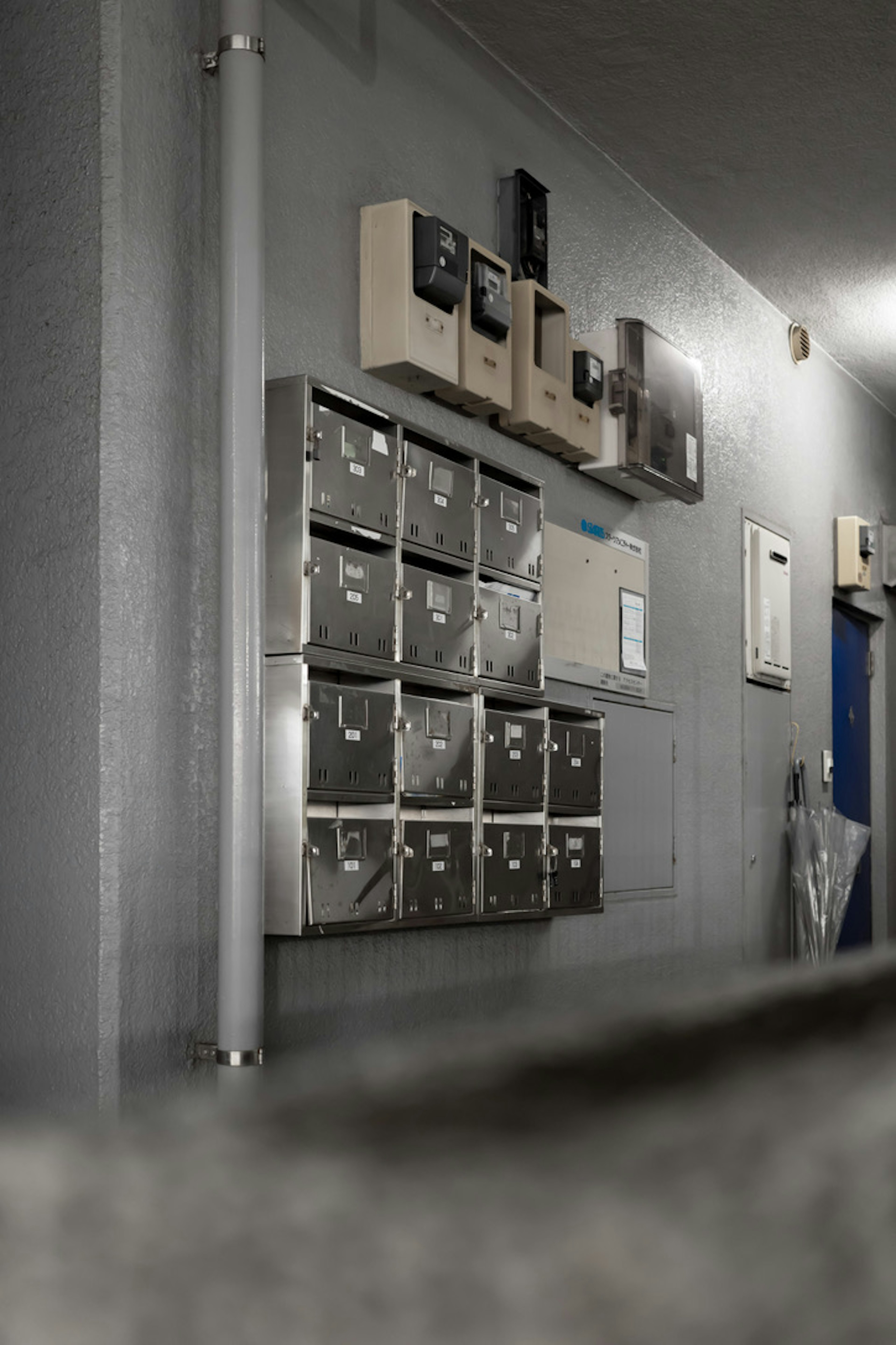 Mailboxes and electrical meter units mounted on a wall in a dimly lit hallway